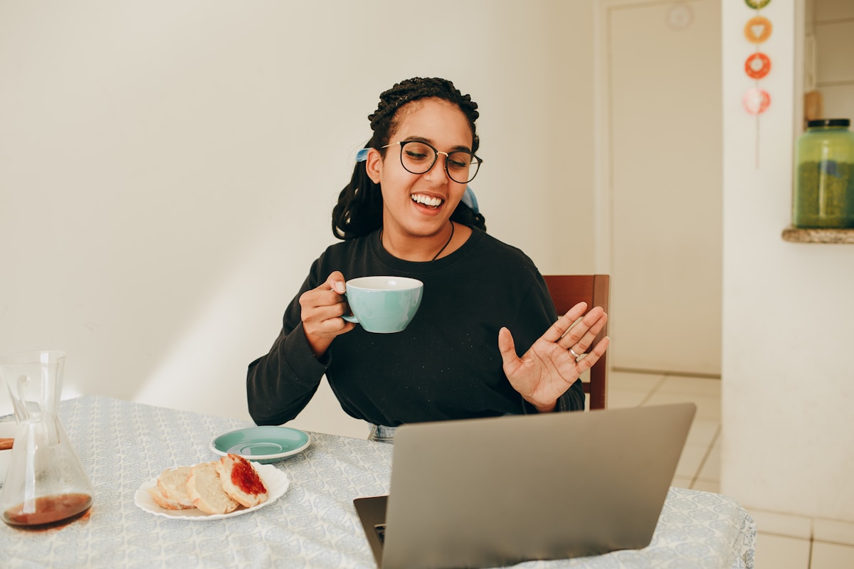A woman smiling during a virtual video consultation at her kitchen table, representing 1-on-1 telehealth visits with a registered dietitian.