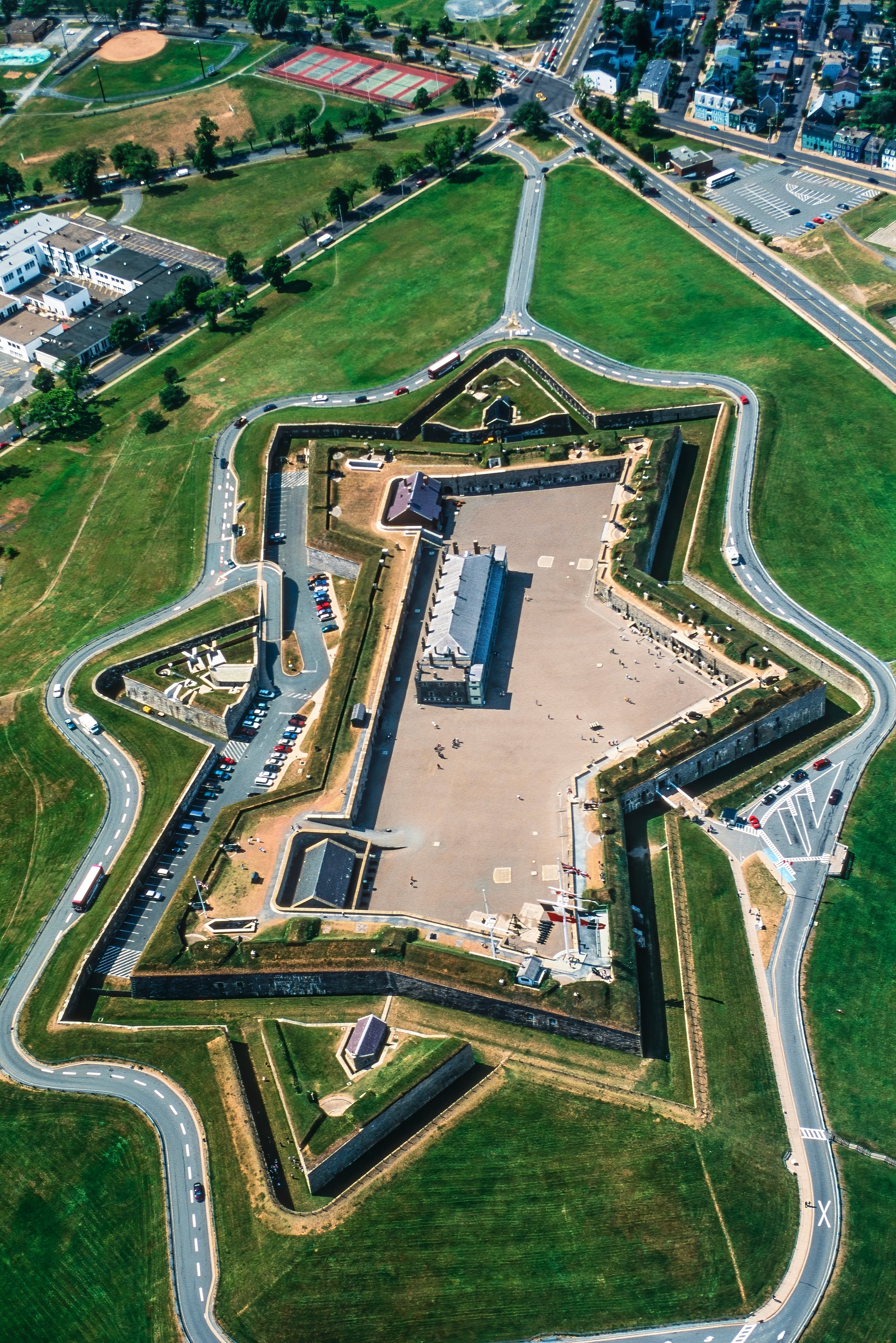 A young person with curly hair smiles at the camera while sitting in front of a laptop against a dark background.