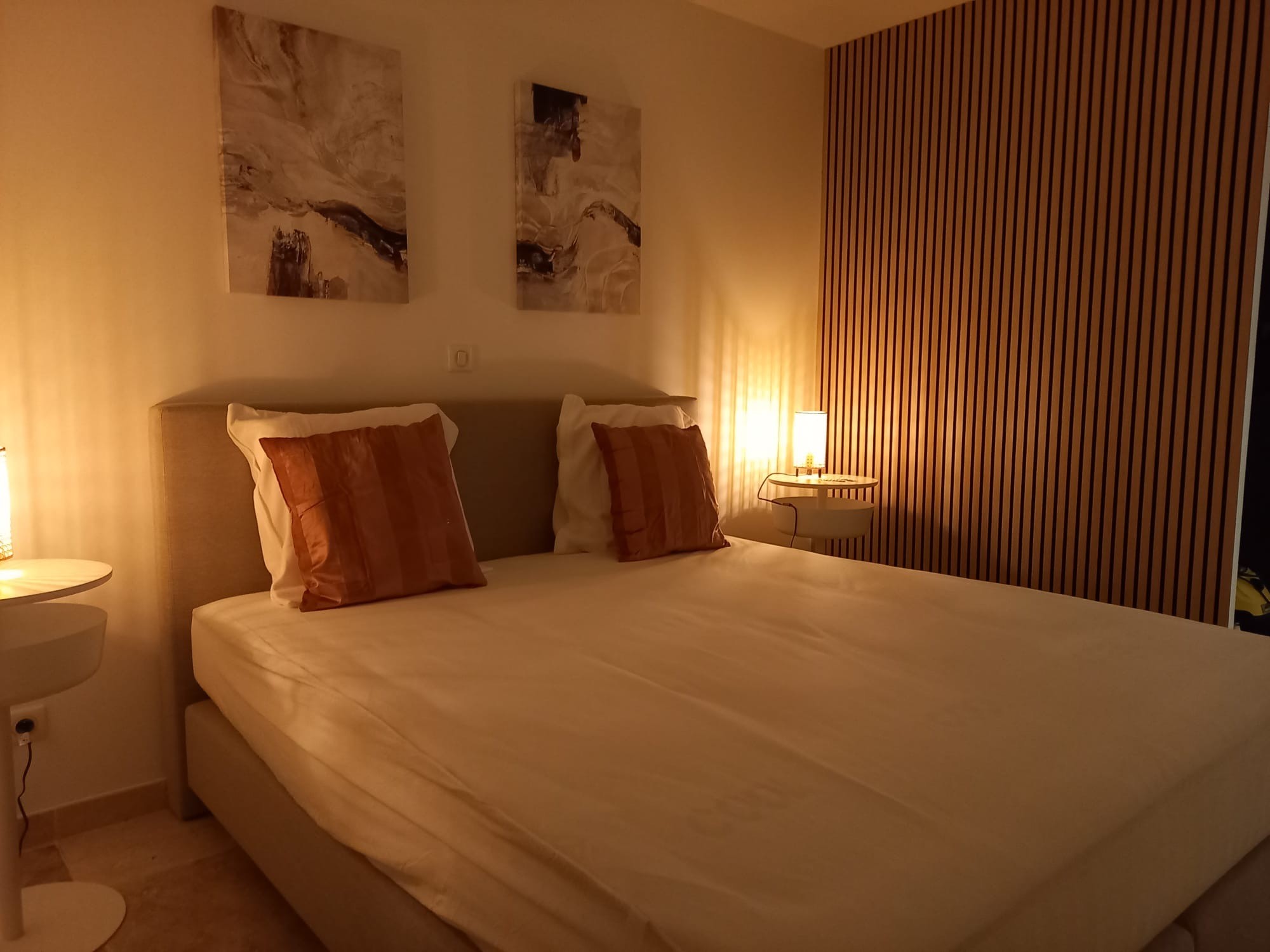Chambre moderne et chaleureuse avec lit double, coussins orange, et décorations murales