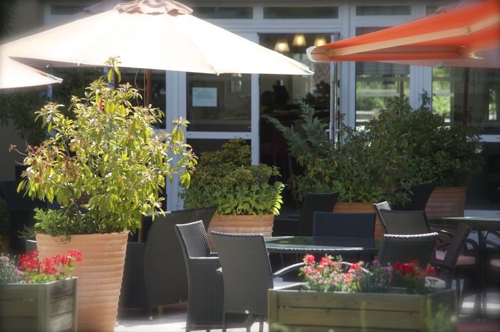 Outdoor terrace with patio furniture umbrellas potted plants and glass-walled entrance area