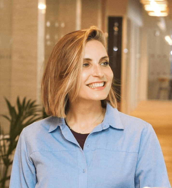 woman in blue dress shirt and blue denim jeans standing beside brown wooden chair
