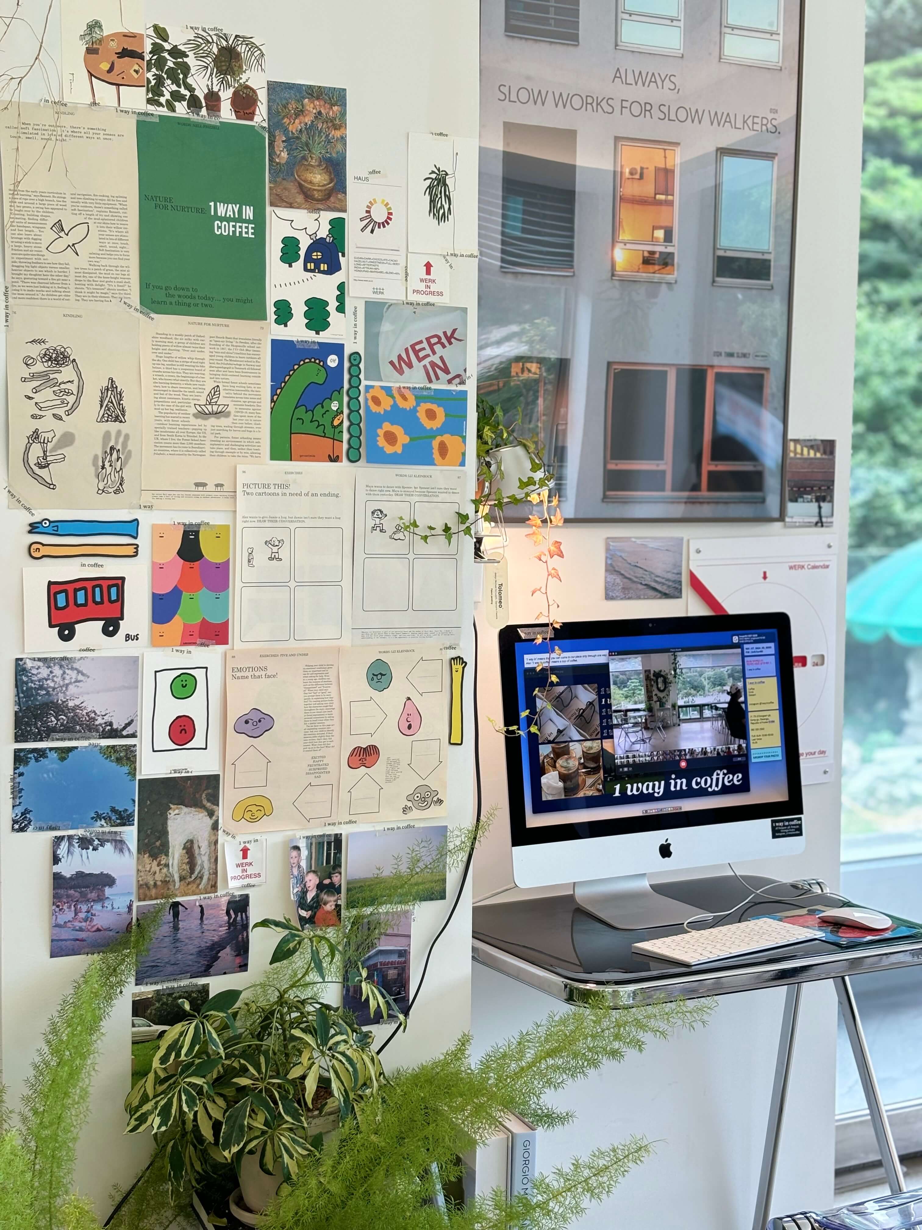 a desktop monitor set against a busy wall covered with design inspiration clippings and next to a fern