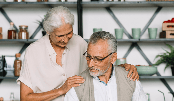 Smiling elderly couple embracing in a kitchen. Woman with white hair touches man's shoulder.