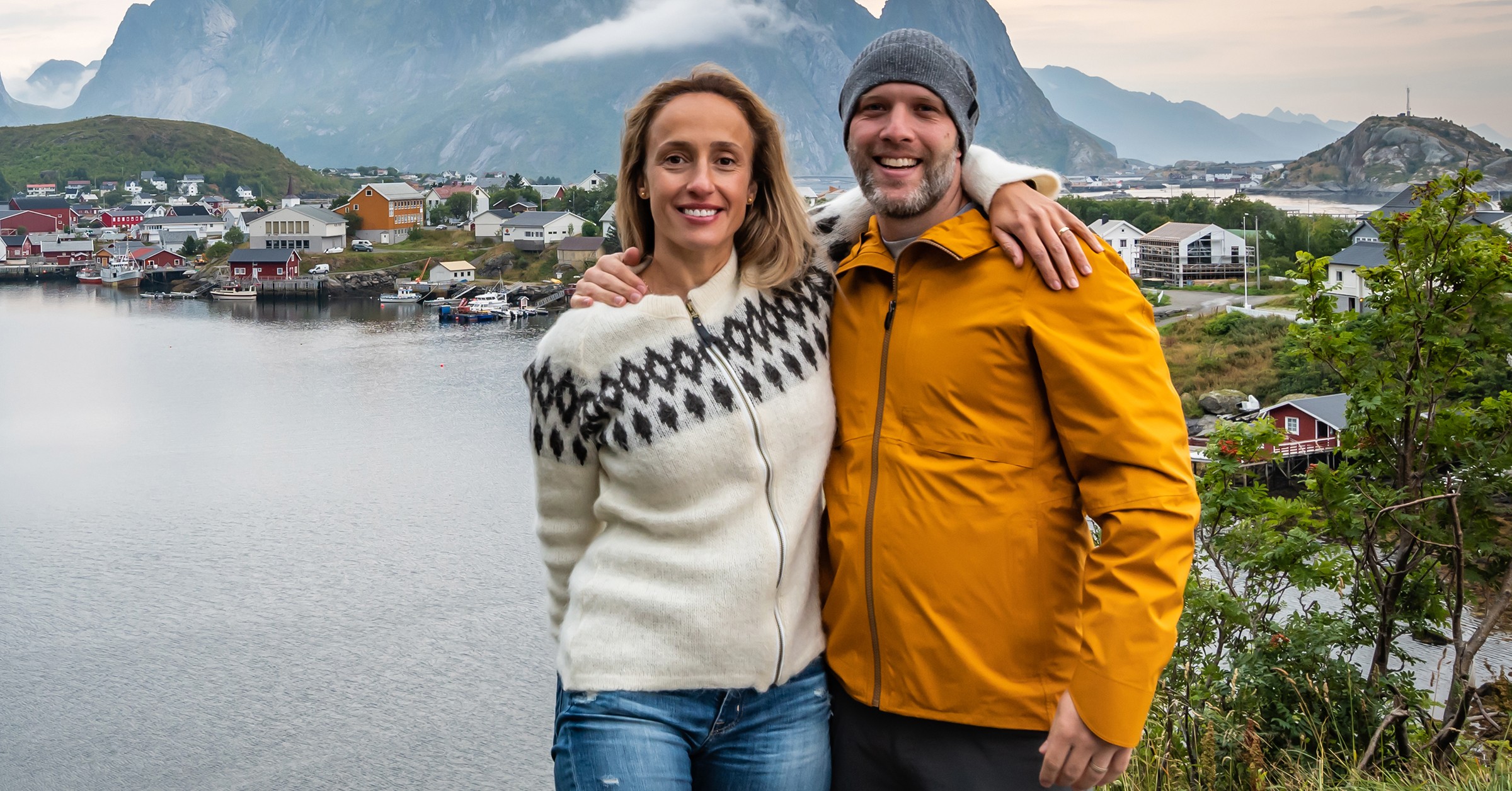 Ett lyckligt par står och håller om varandra med en norsk utsikt i bakgrunden.