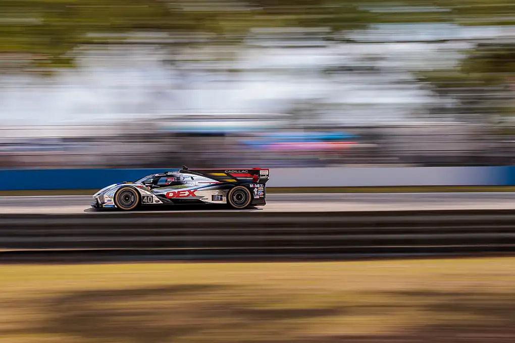 A reflective silver Cadillac race car zooms along a track, emphasizing its speed and striking appearance against the backdrop of the circuit.