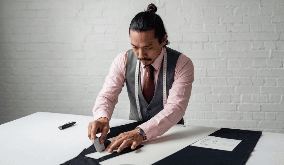 Custom suit vs suit alterations guide showing a tailor measuring and cutting fabric at a worktable