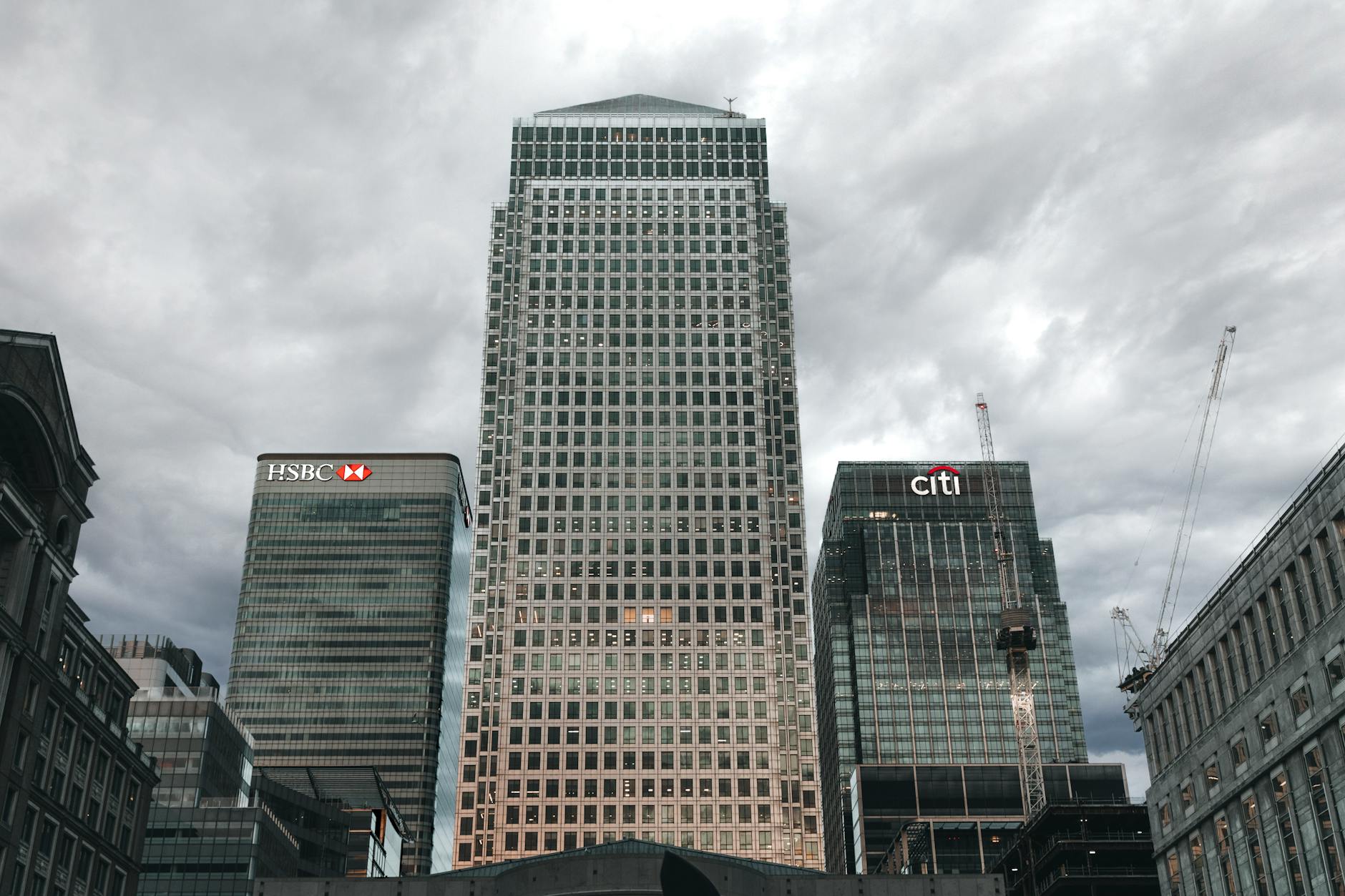 Canary Wharf skyline showing One Canada Square between HSBC and Citi towers under a heavy grey overcast sky.