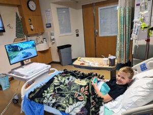 A patient enjoys playing Forza on a GO Kart while resting in a hospital bed.