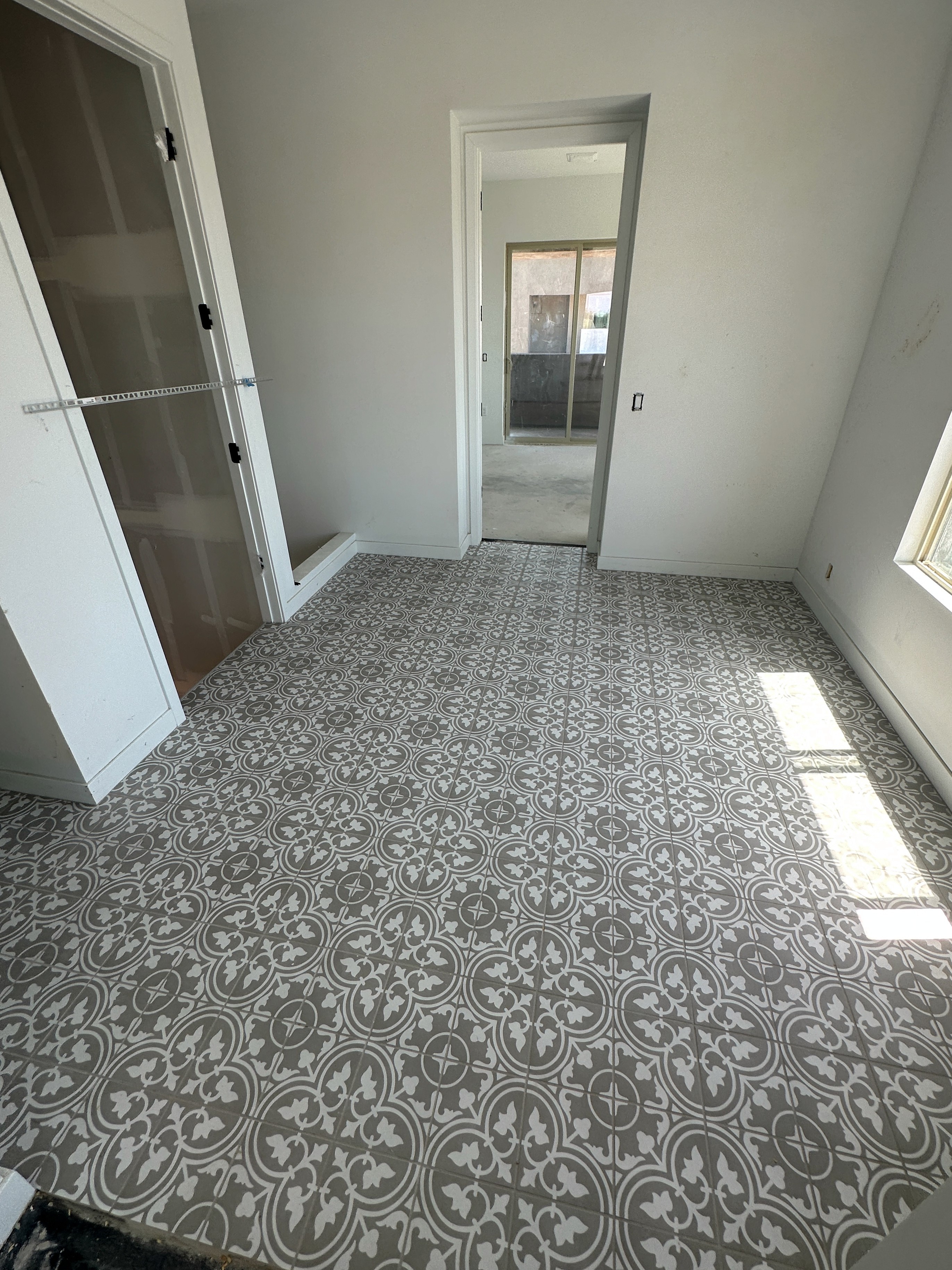 Modern room with patterned tile flooring, white walls, and built-in storage in a new home under construction.
