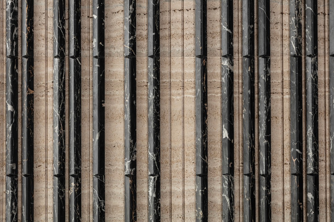Primo piano di sei rotoli verticali di materiale tessile o carta da parati, mostrati di taglio, con texture elaborate in diversi colori, tra cui bianco, nero, grigio chiaro, rosso ruggine e marrone scuro.