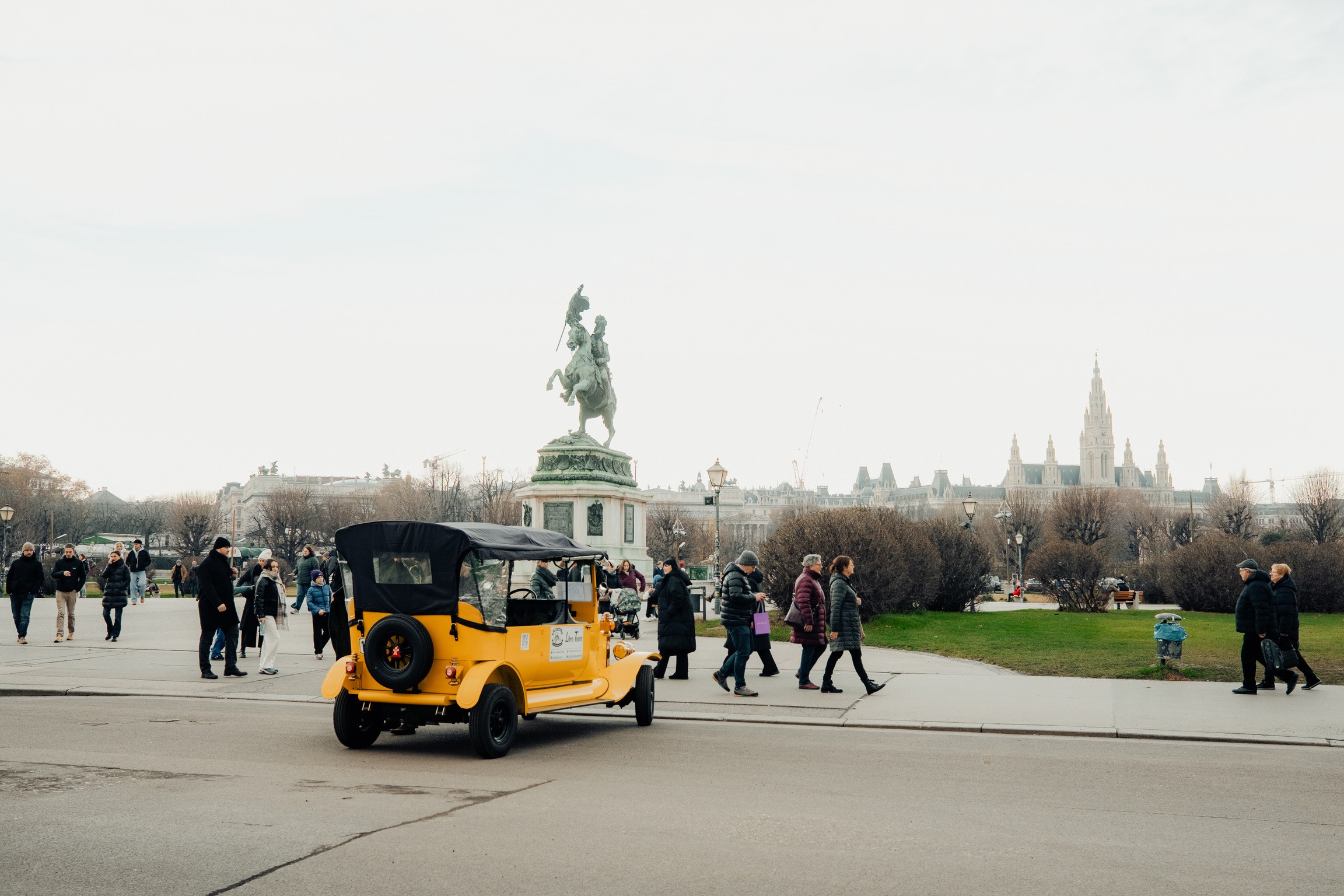 Coche antiguo amarillo en la Heldenplatz con la estatua ecuestre y el Ayuntamiento al fondo