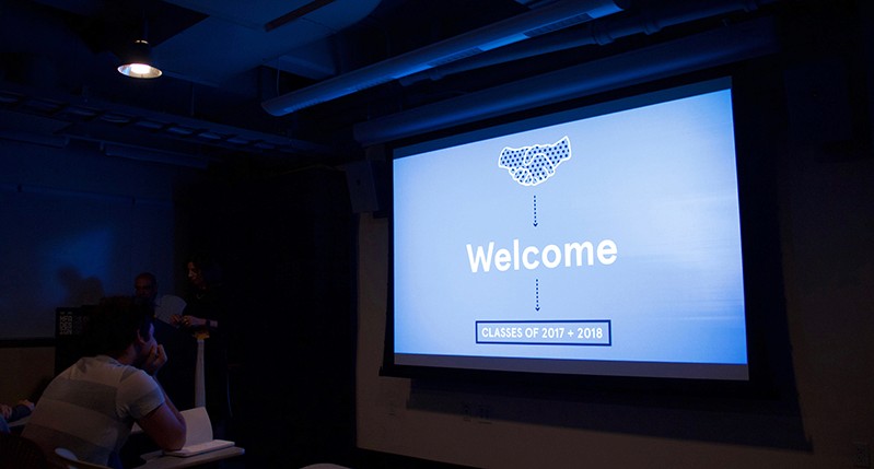A photo of a screen projector showing a blue image, an icon of two hands shaking, the word Welcome and some date and time.