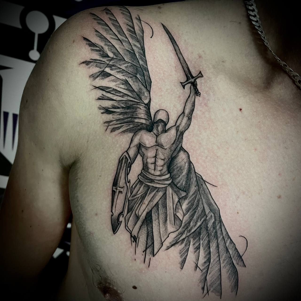Wytatuowana na klatce piersiowej anioł stróż z mieczem. tatuaż czarno-szary Szczecin