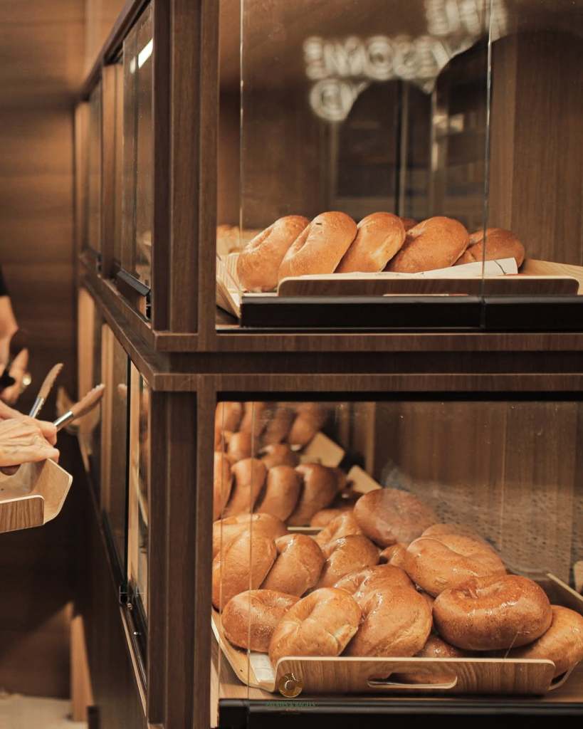 A display case featuring freshly baked bagels on wooden trays, with a person holding a serving tray nearby.