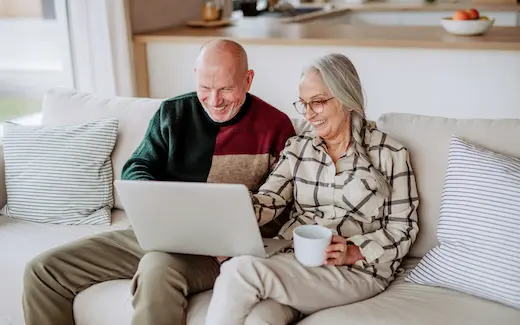 A photo of an elderly couple smiling as they look at their investments on a laptop