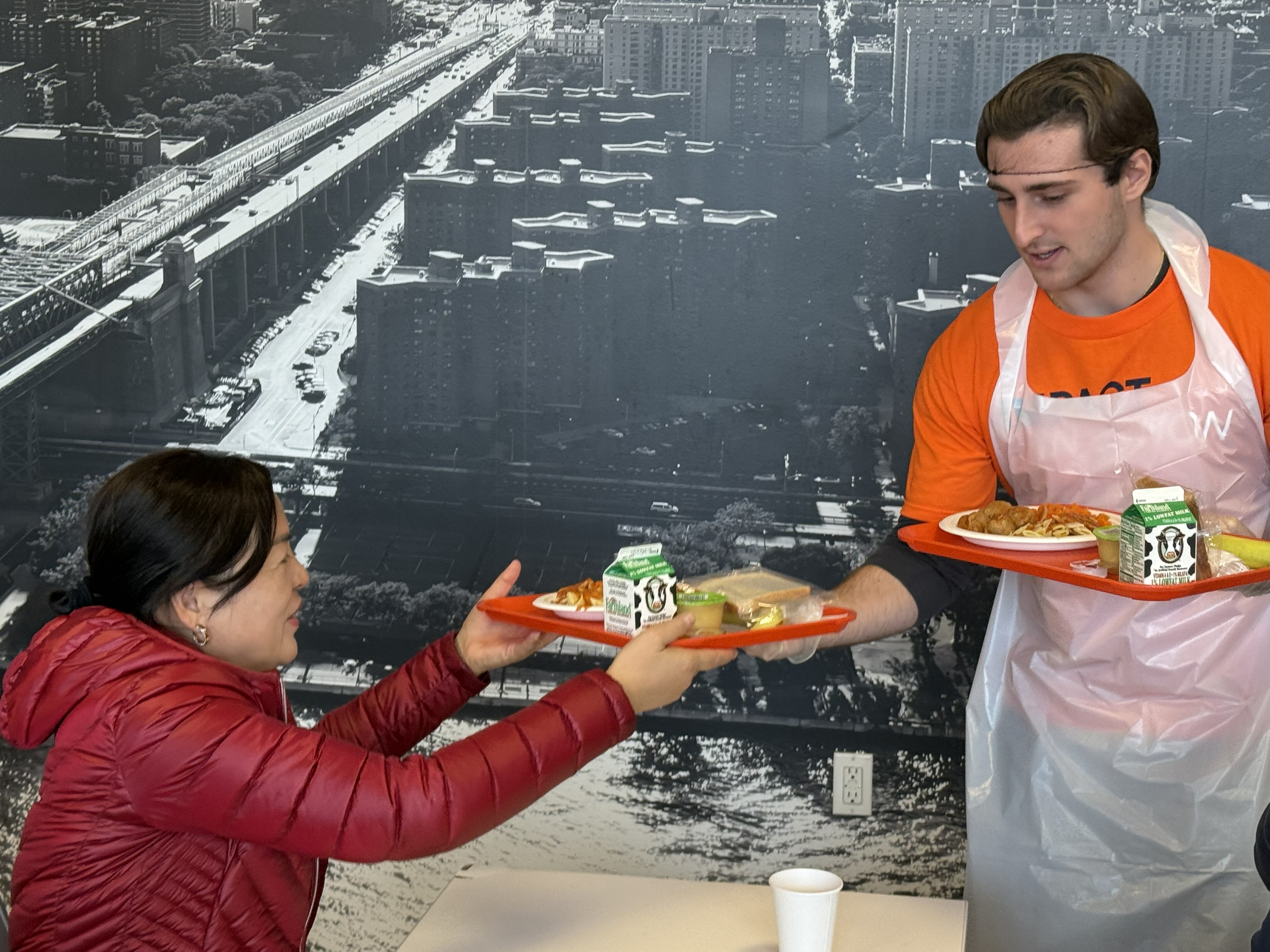  A volunteer, dressed in kitchen wear, passes a lunch tray to a woman. 
