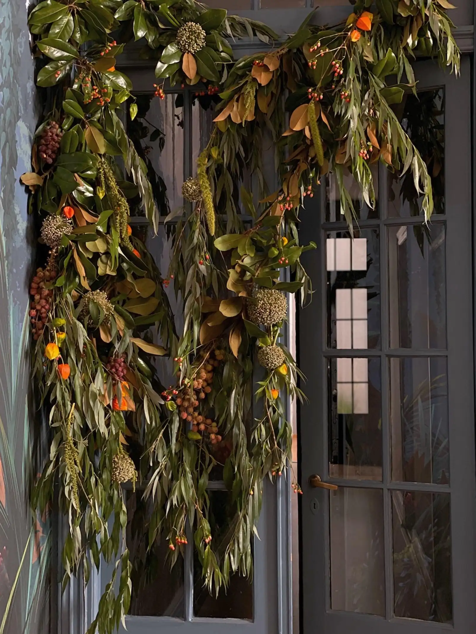 Guirnalda botánica con follaje verde y frutos otoñales sobre puerta antigua para decoración de interiores natural.