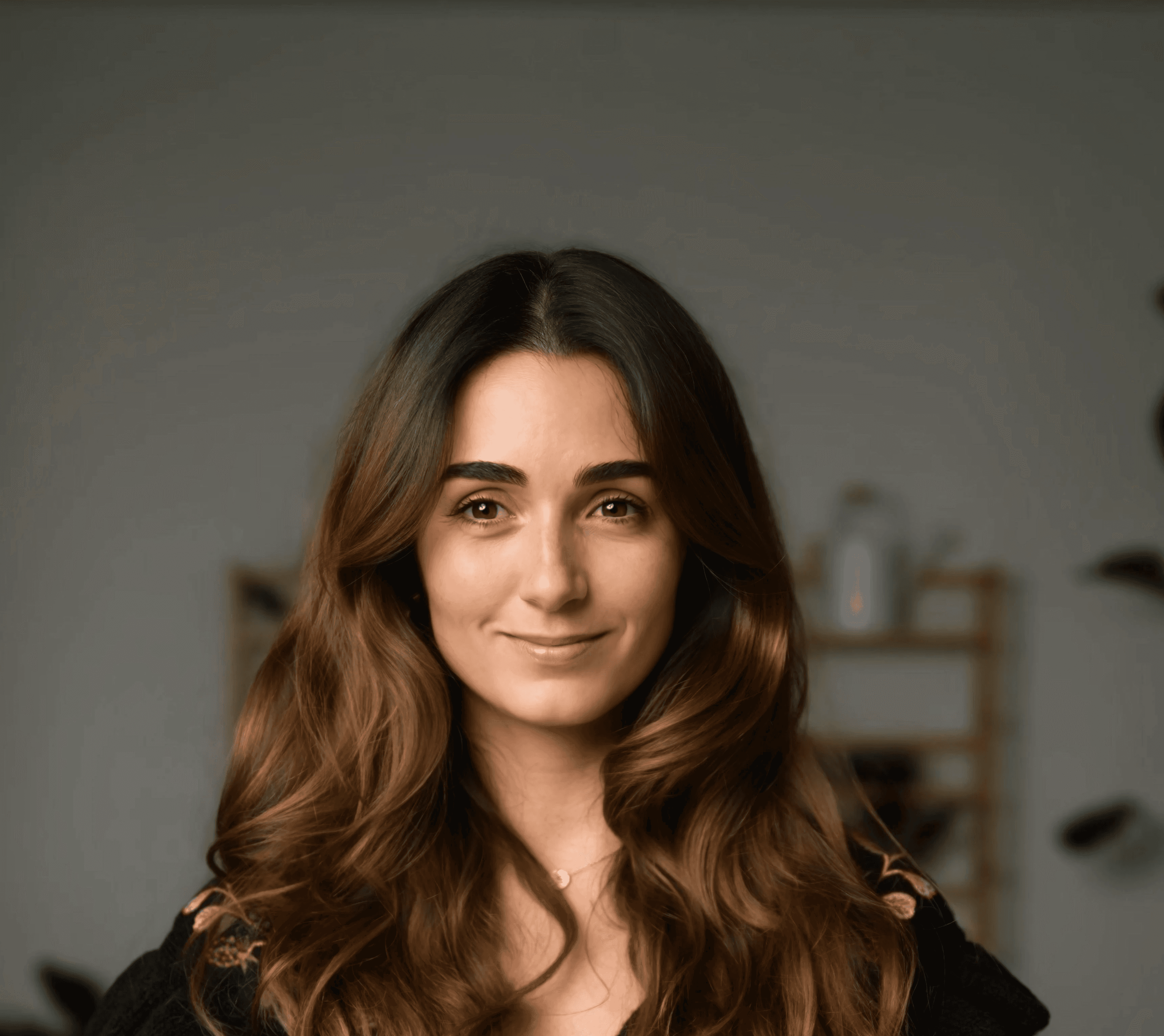 A smiling woman with long, wavy brown hair, wearing a dark top against a soft gray background representing an author for.