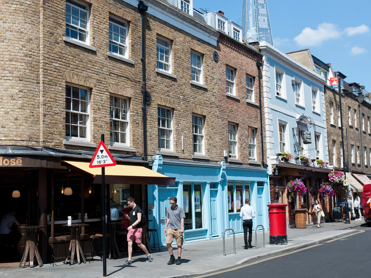 A smiling man with curly hair is sitting at a desk, looking at the camera, with a laptop and a lamp in the background.