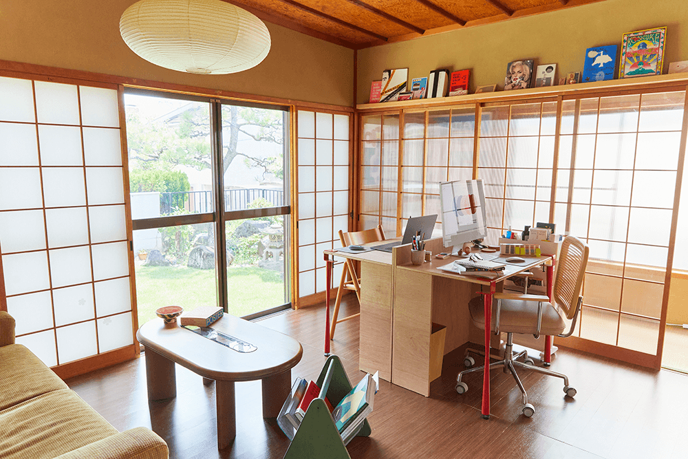 Josephine Grenier’s design studio in a Japanese-style room with shōji panels, a wooden desk setup and design books on a high shelf.