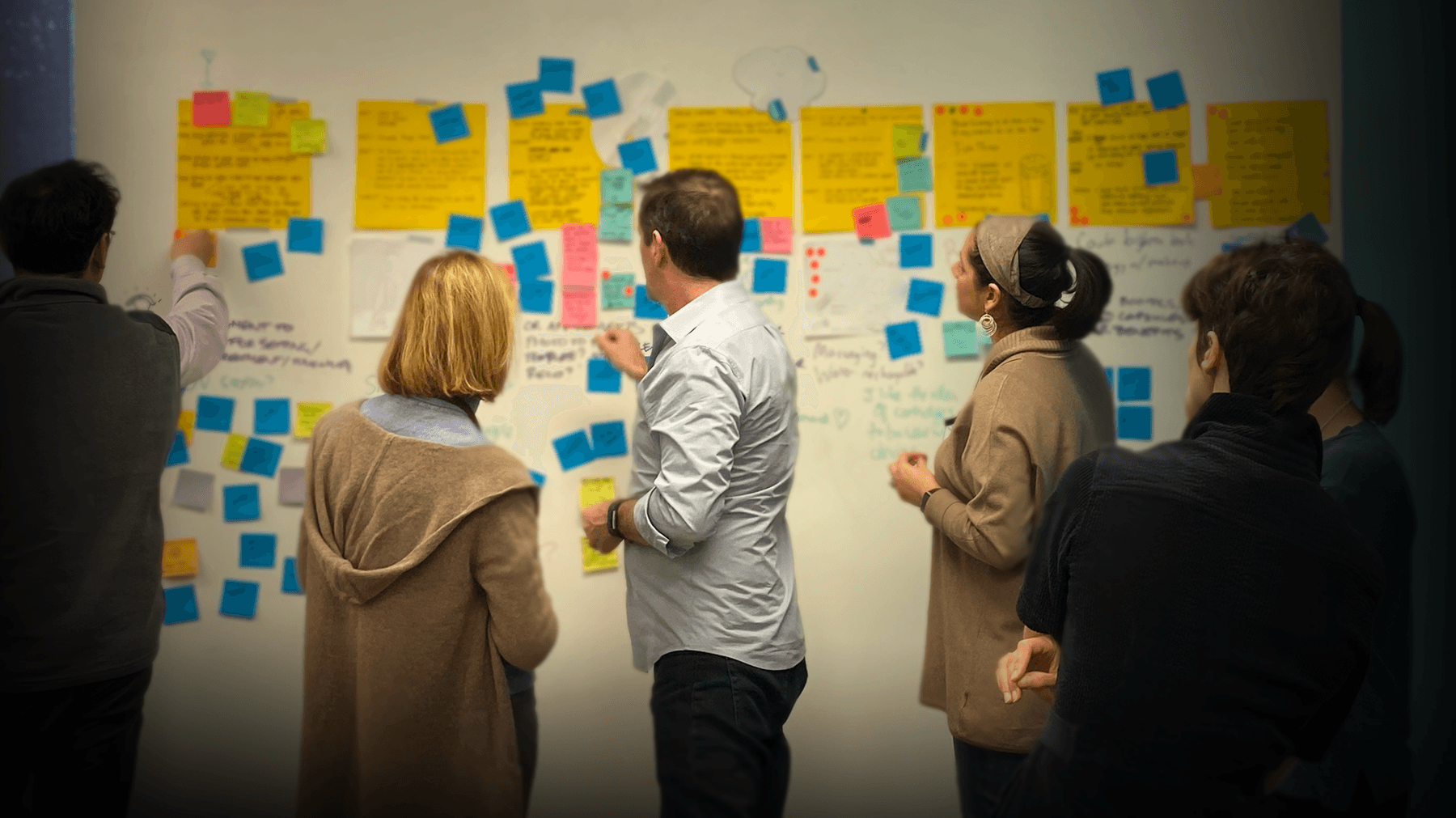 Leaders collaborating in a human-centered, data-driven transdisciplinary design thinking workshop, talking with sticky notes that guide product and service transformation.