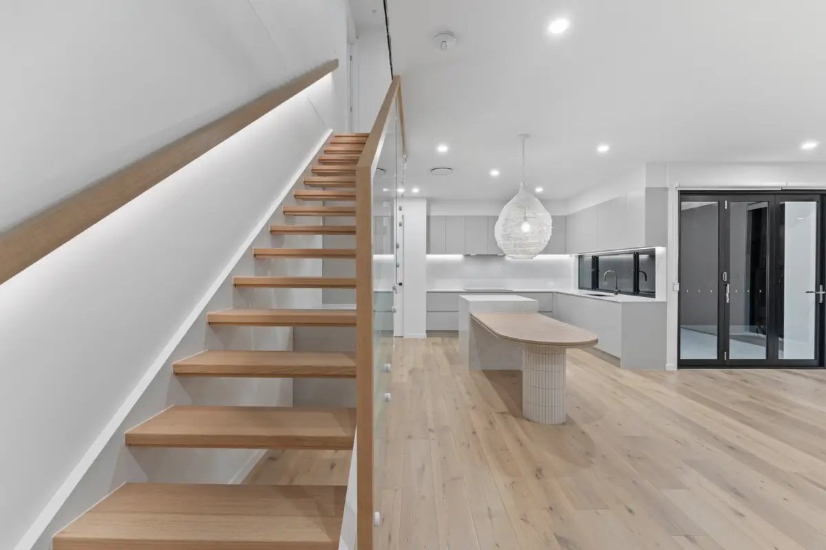 Modern home interior featuring light wood stairs, an open-plan kitchen with an island, and light wood flooring.