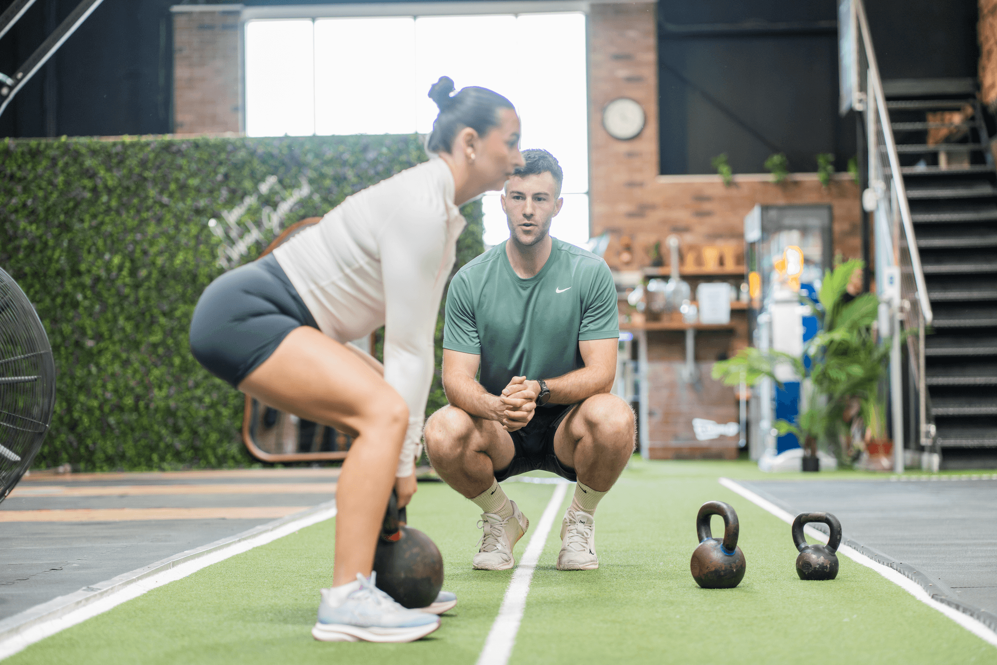 Woman lifting a kettlebell in a moder gym with a personal trainer