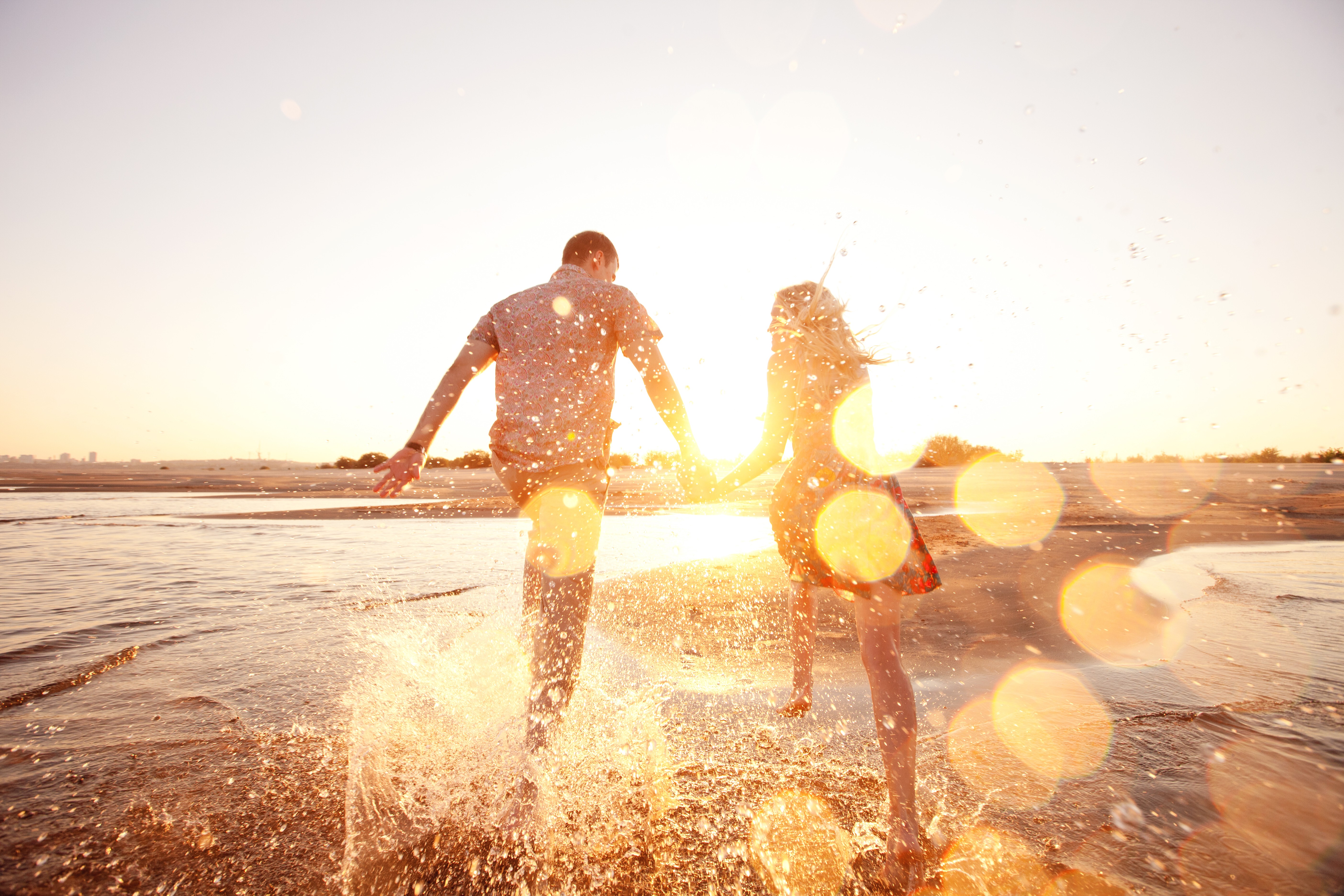 A happy couple splash at the beach in sunset