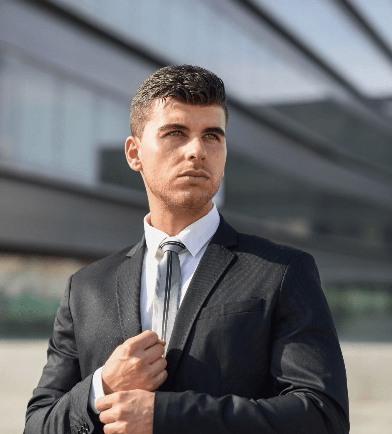 A handsome man in a sharp black suit adjusting his cuff outdoors