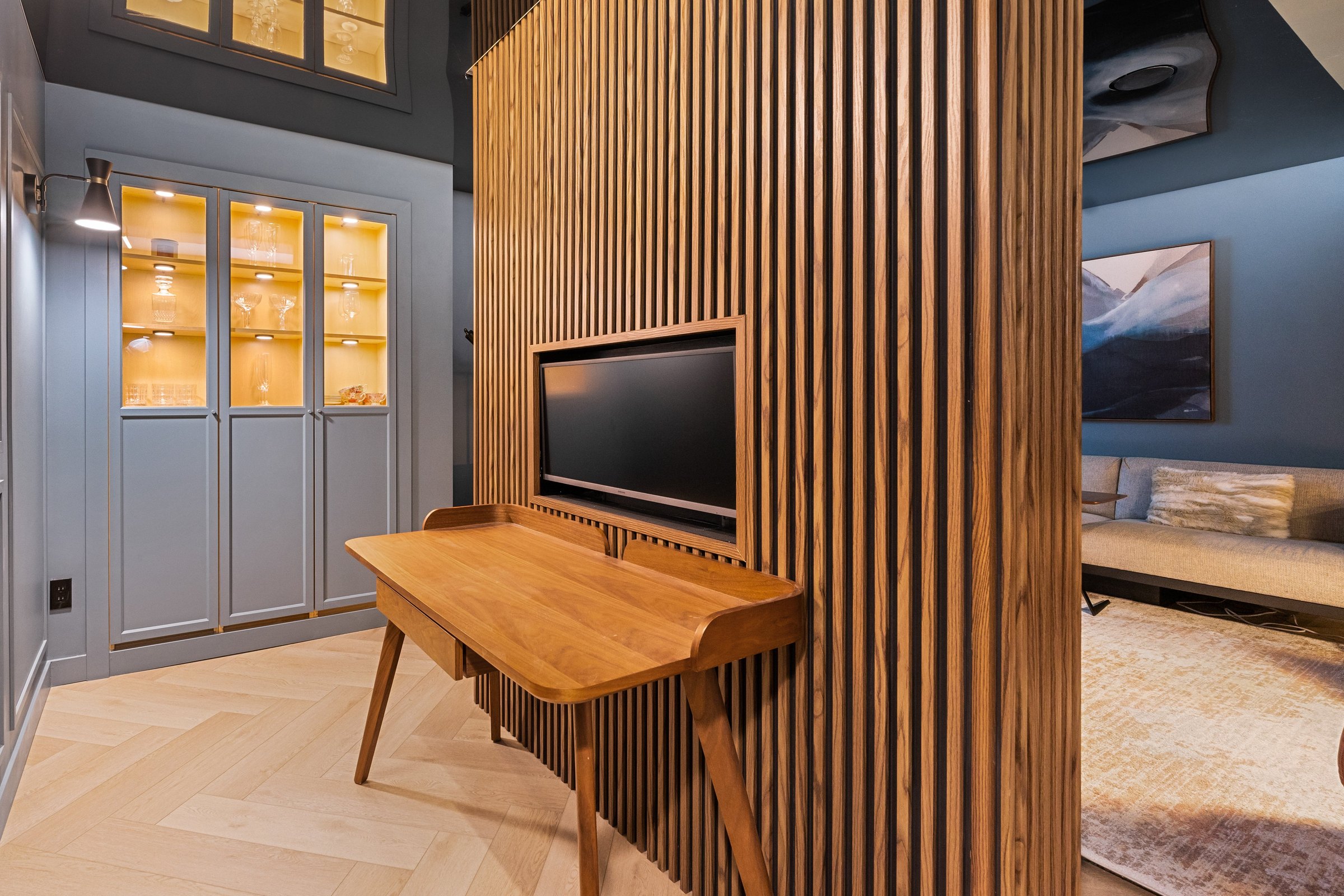 Crestmont basement finished: walnut desk against the slatted wall, with lit glass-front cabinets beyond