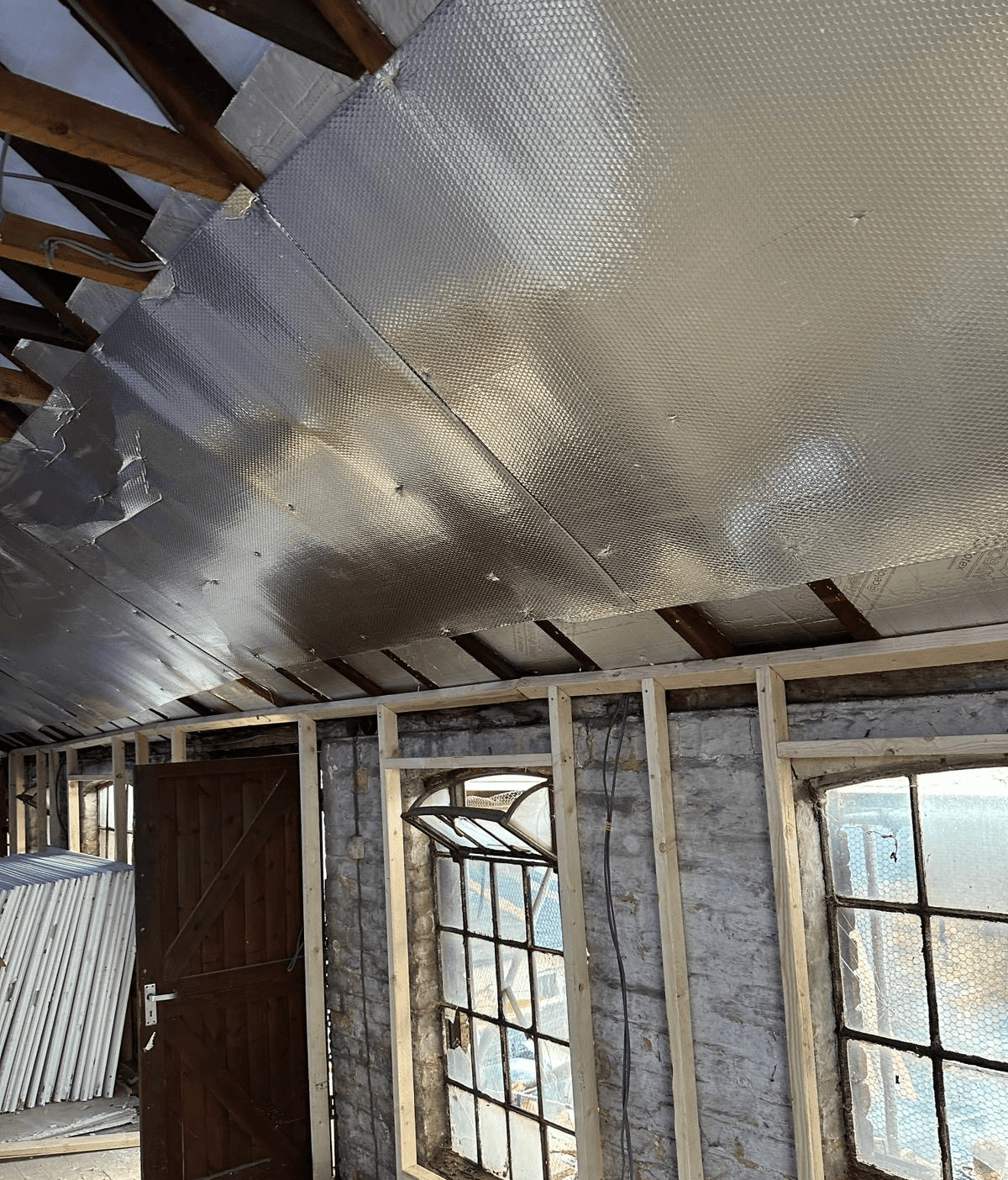 Foil-backed roof insulation installed beneath timber rafters during building refurbishment