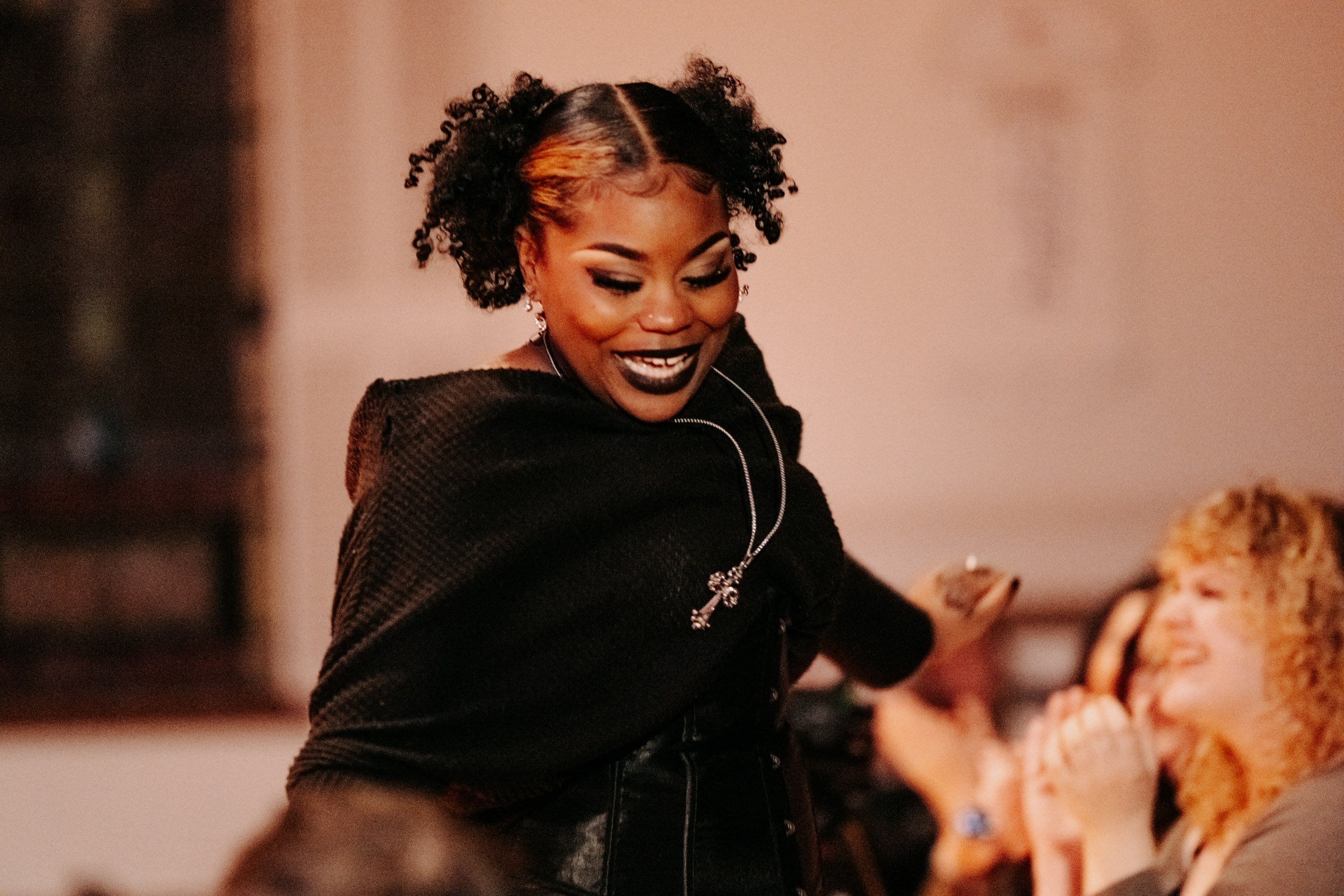 Performer smiling and engaging with the audience during the Queer Open Mic (QOM) hosted by be; community in Bridgewater, Massachusetts