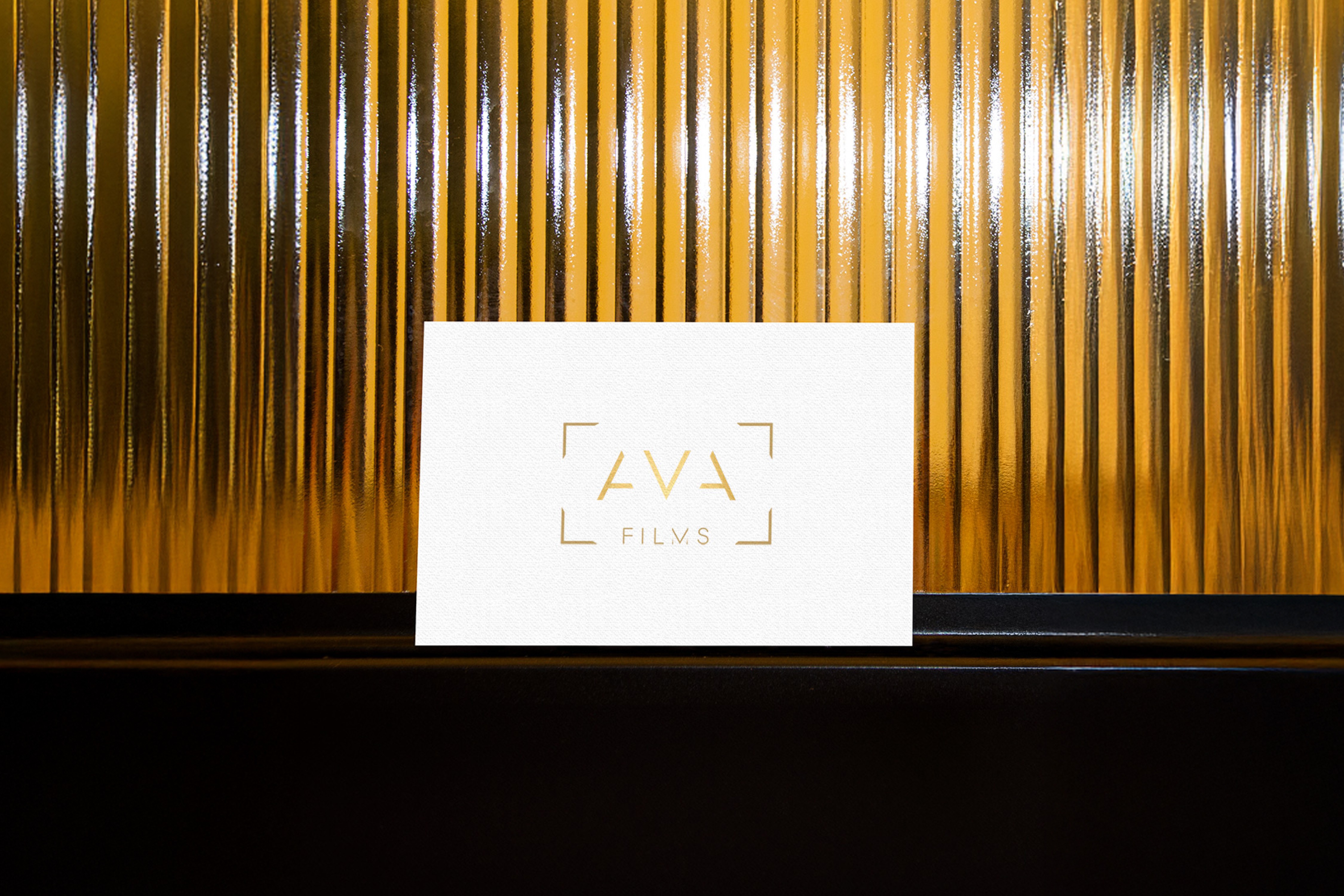 Elegant white AVA Films business card with gold foil logo, set against a golden metallic backdrop, exuding a refined and upscale brand identity.