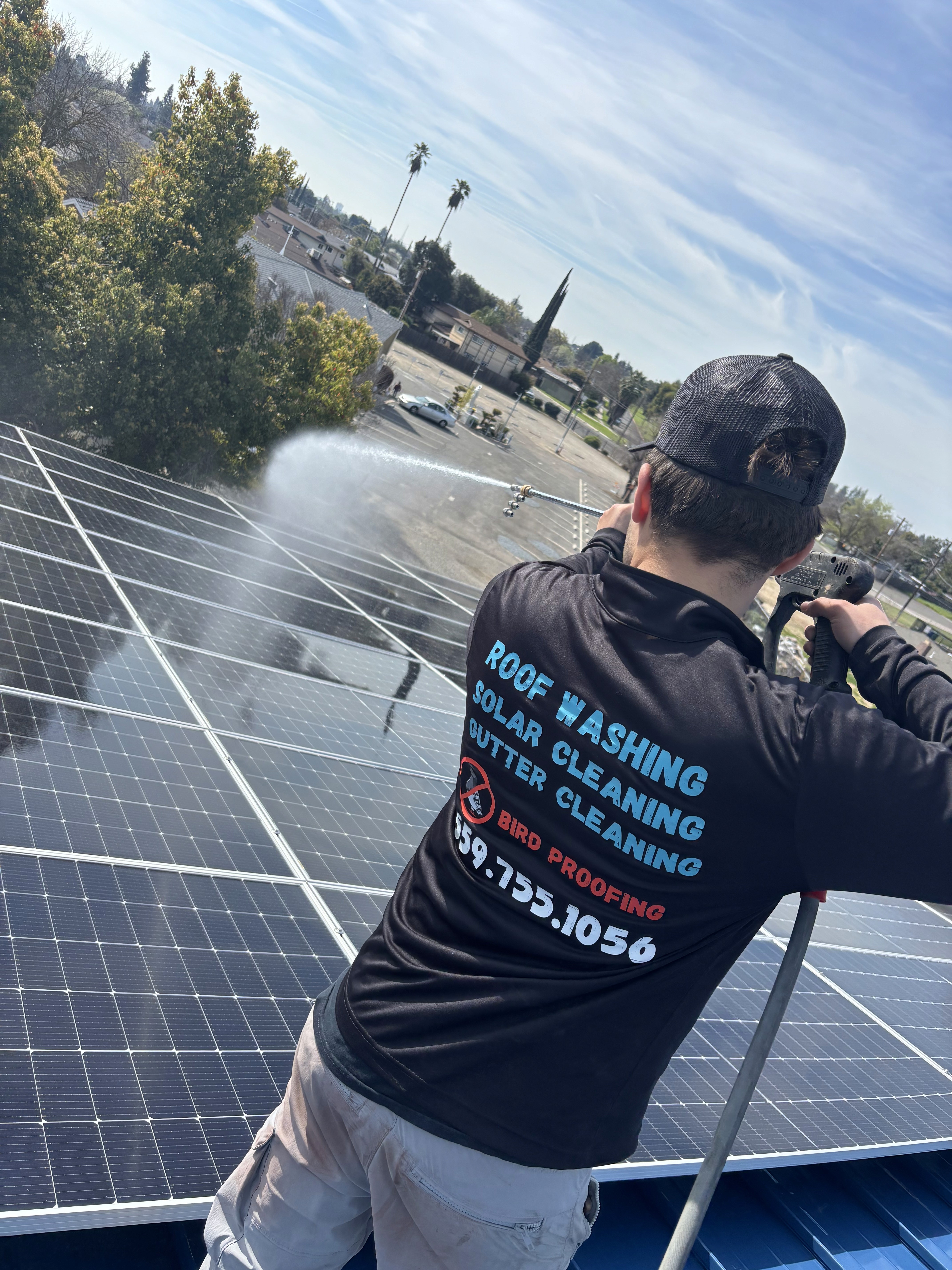 Technician pressure washing commercial solar panels on a rooftop to clean dirt and improve energy production