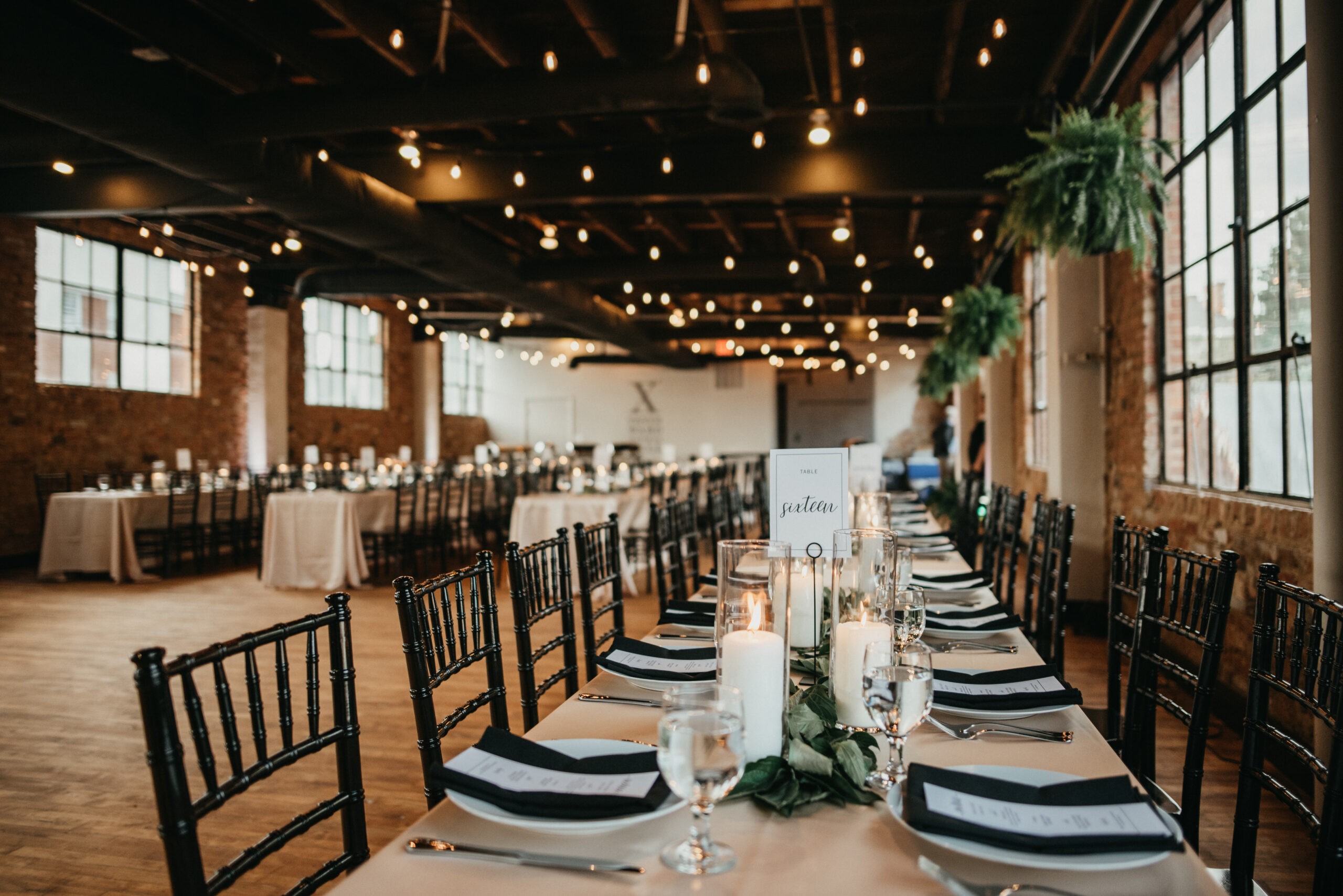 A serene outdoor wedding setup with white chairs arranged on green grass under a canopy of trees.