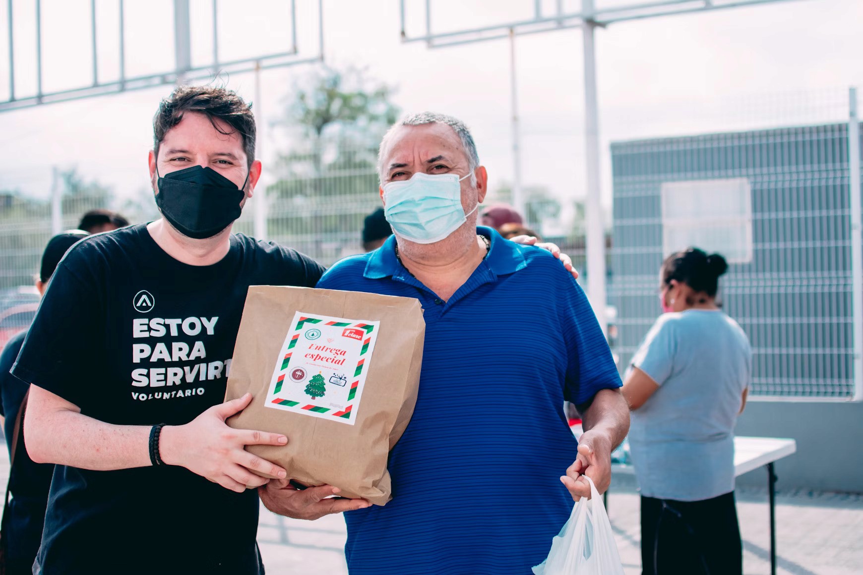 Volunteers distribute food packages during a community event wearing masks.