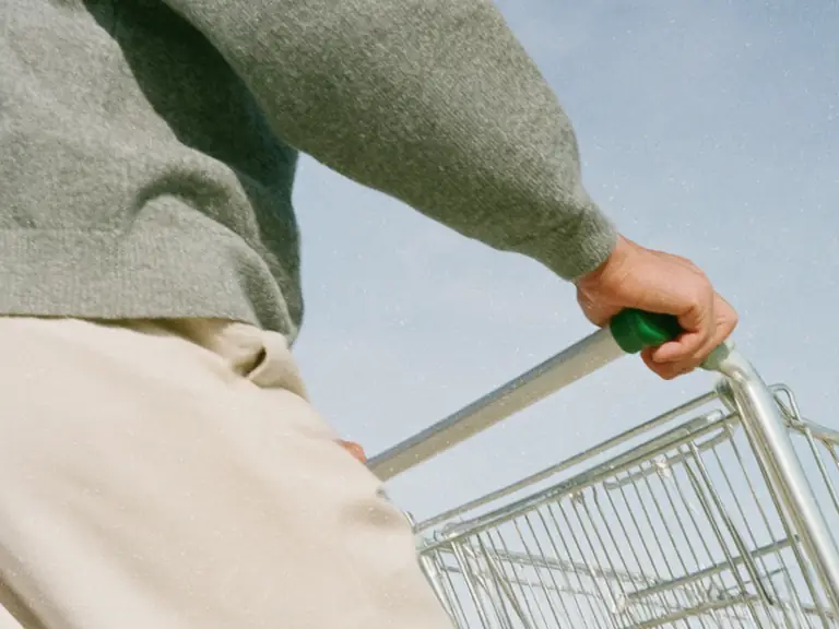 Person pushing a shopping trolley beneath a blue sky.