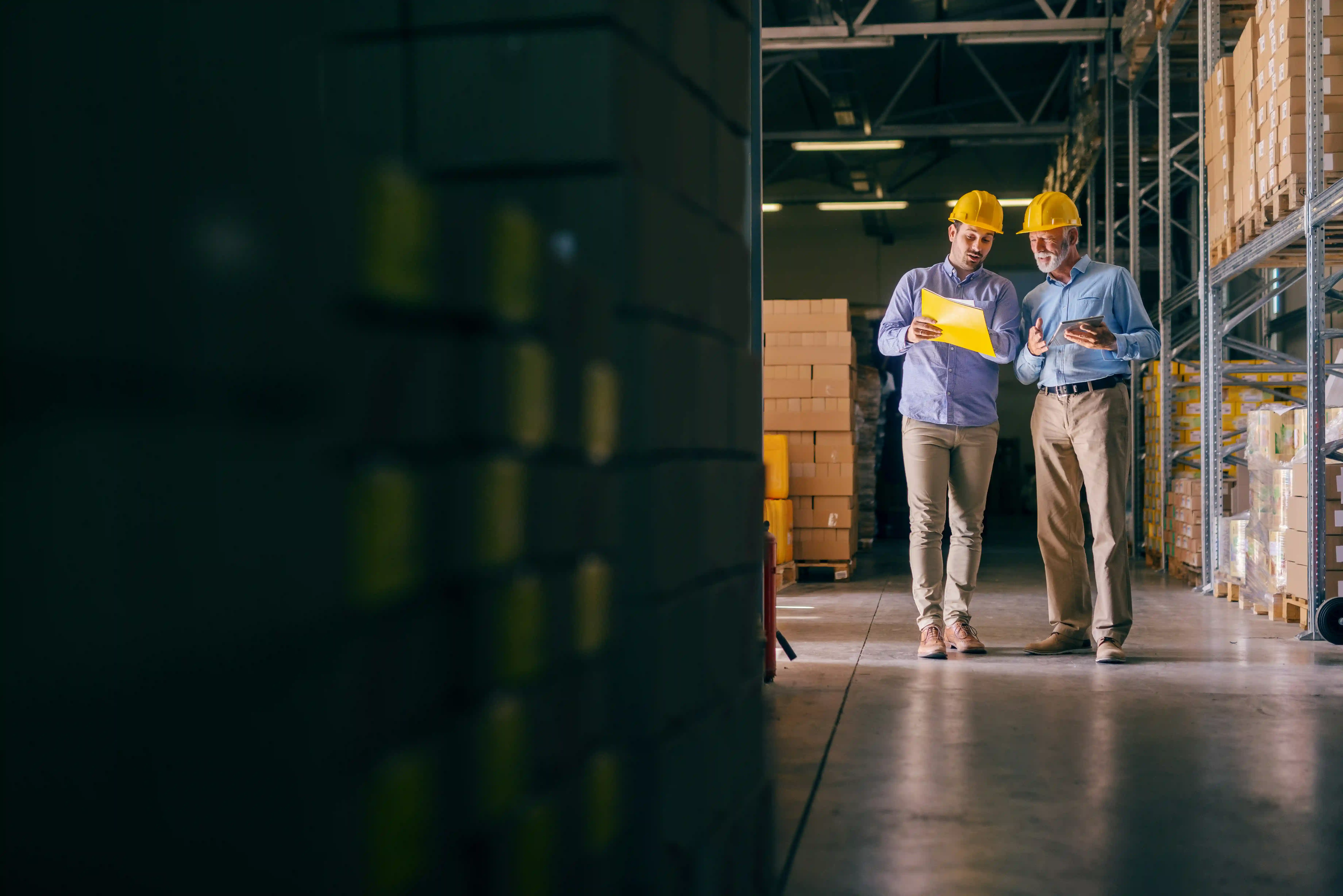 two men in yellow hard hats and blue shirts walking around the inside of a 3PL warehouse