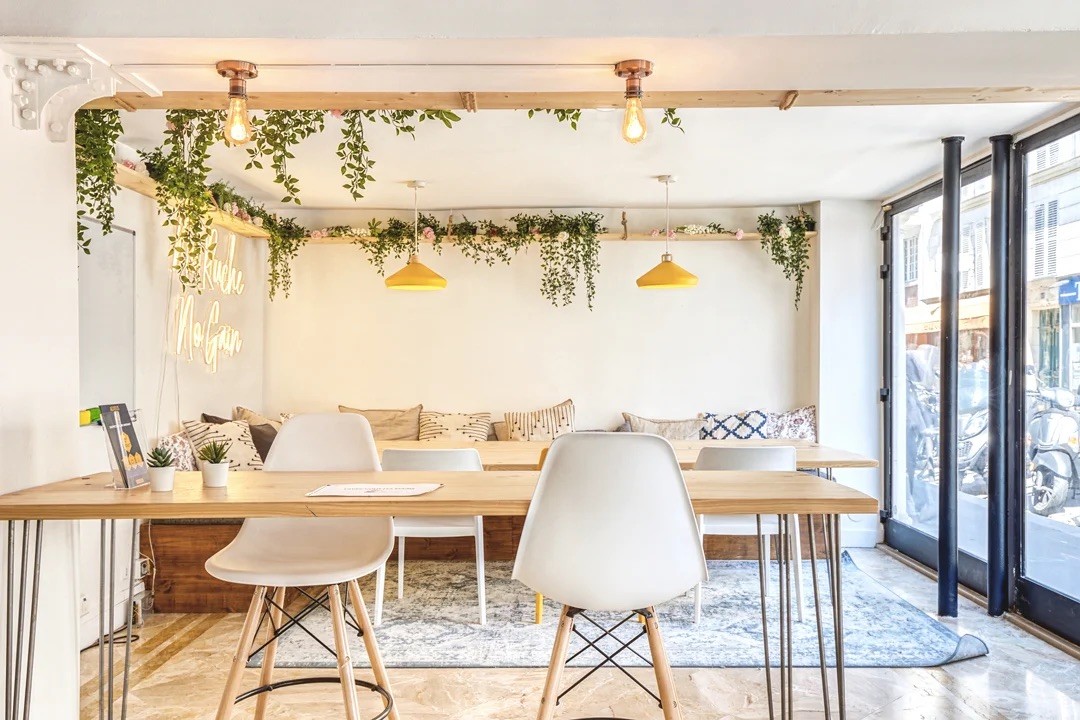 Bureau partagé lumineux avec chaises blanches modernes, grandes baies vitrées et plantes vertes suspendues.