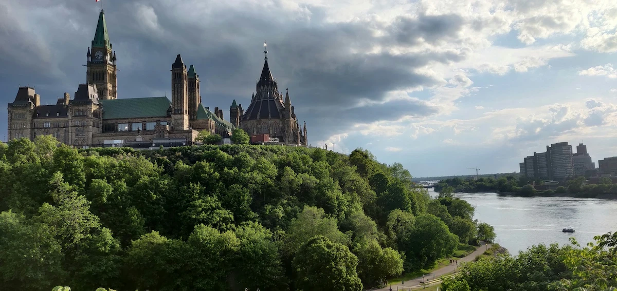 Parliament Hill overlooking the Ottawa River, Canada, surrounded by lush green trees.