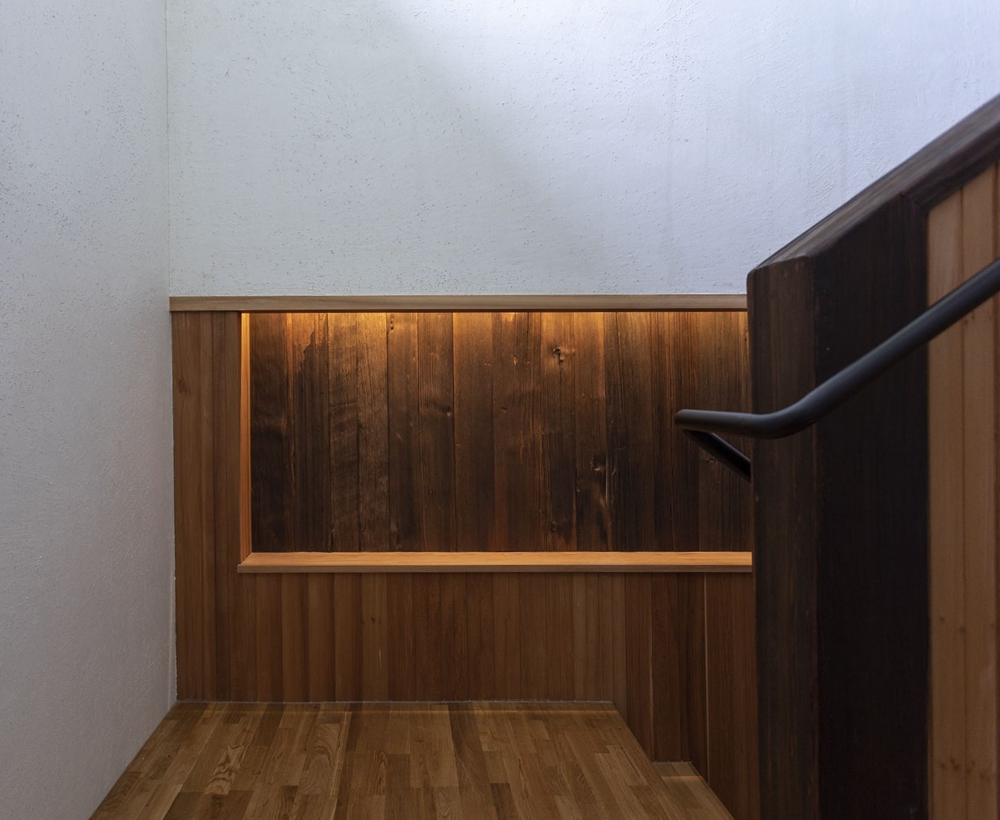 樓梯轉角處設計間接照明木質牆面，牆面深淺木紋對比強化材質層次感