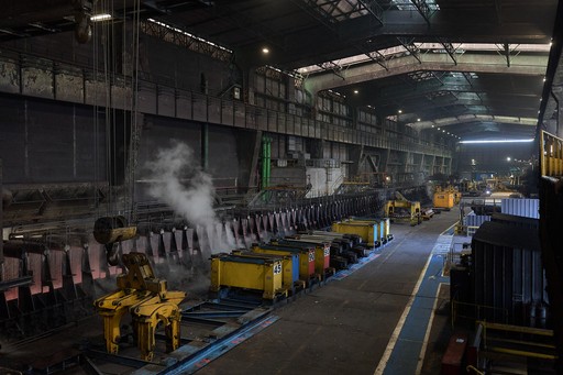 Vue grand-angle d'un hangar industriel ArcelorMittal, avec de la vapeur d'eau qui émane des brames d'acier refroidi par des jets d'eau.