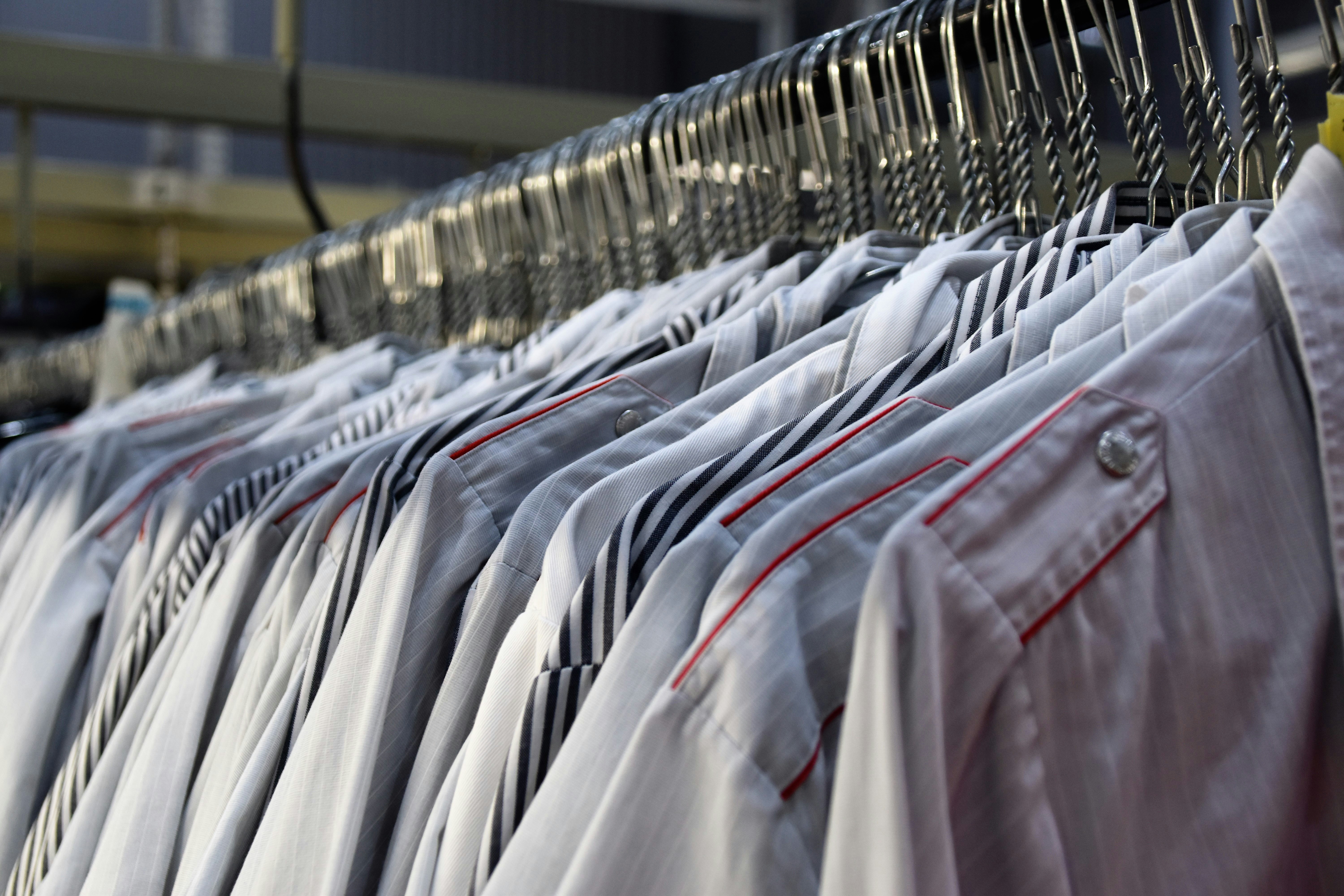 Row of neatly hung white dress shirts with striped ties on metal hangers in a clothing store or warehouse.