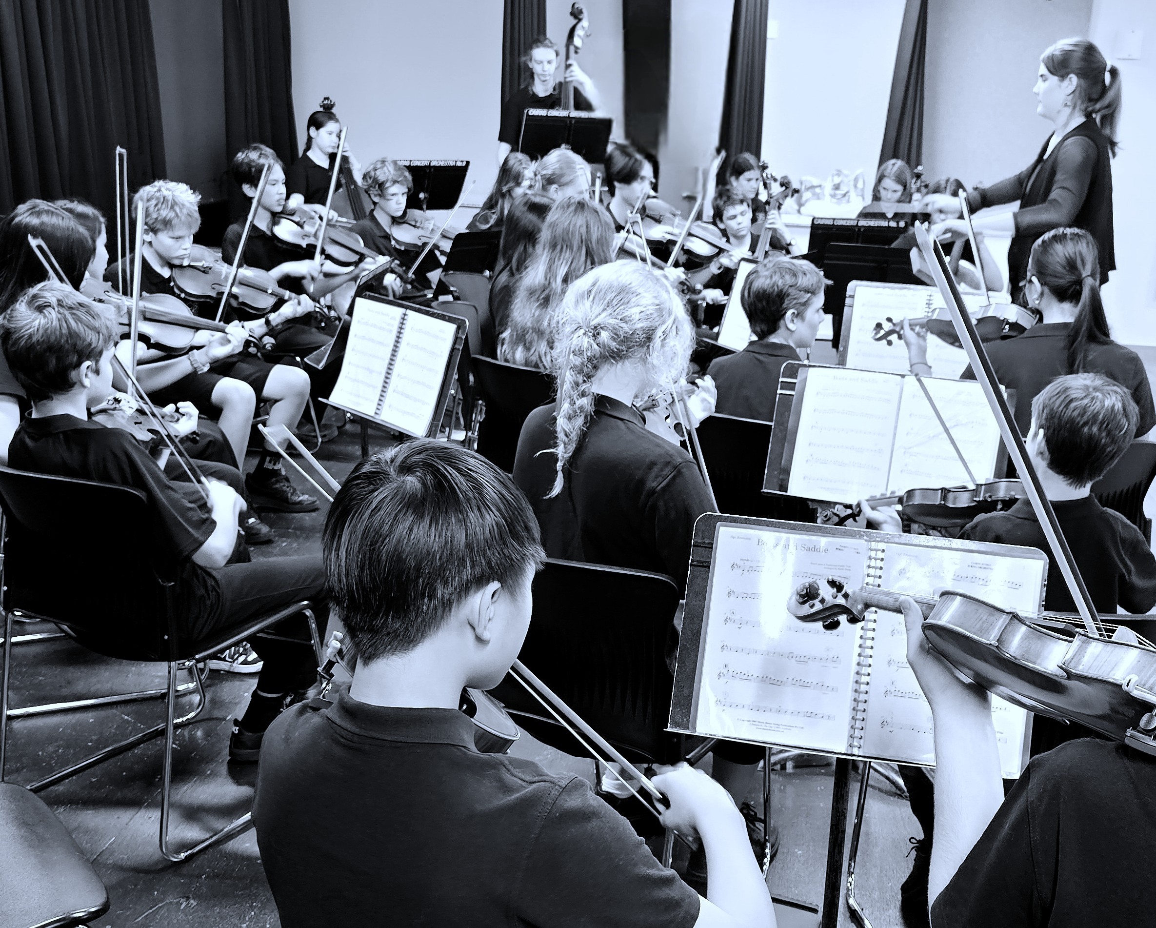 Cairns String Orchestra conductor leading youth musicians during indoor rehearsal, black and white