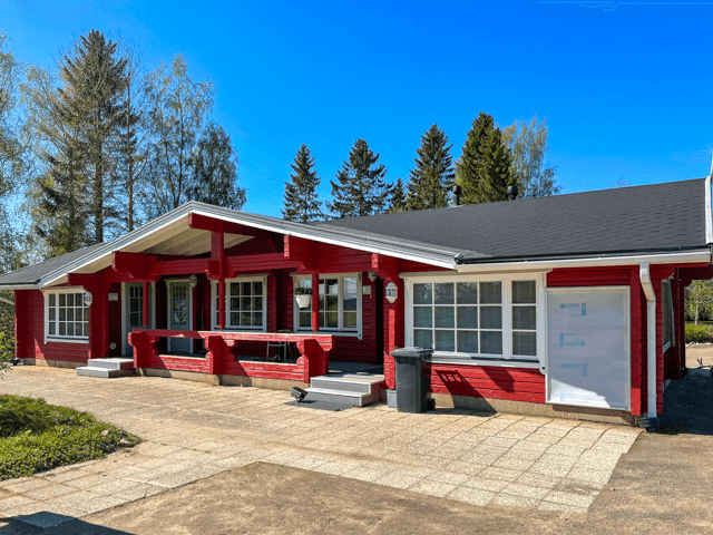 Ulkomaalattu punainen hirsirakennus Seinäjoella, laajalla katetulla terassilla, kivetty etupiha