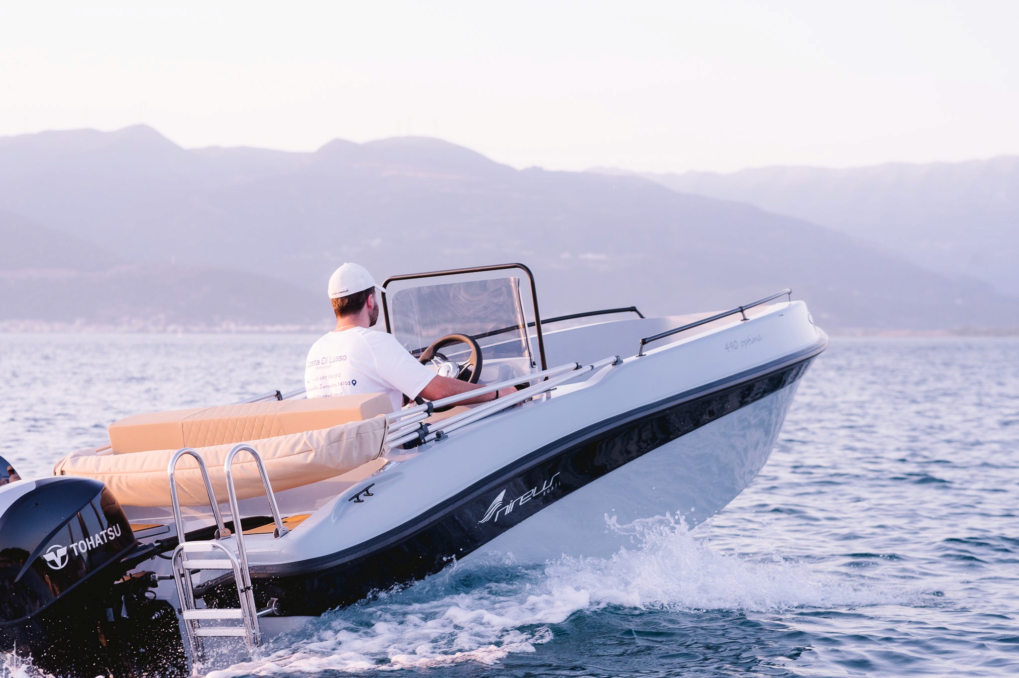 Captain steering white Nireus speedboat through choppy blue waters with mountainous Cycladic coastline in background