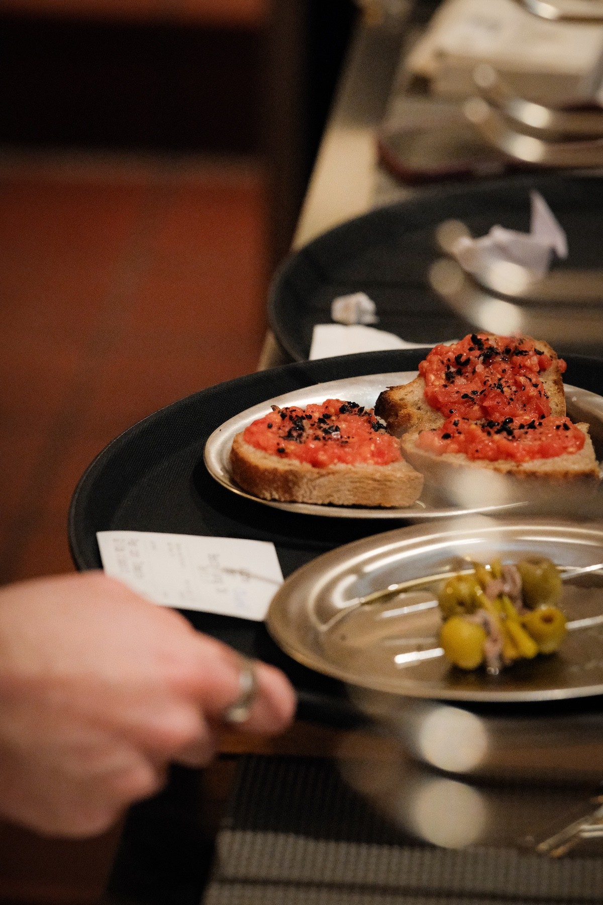 Mitarbeiterin einer Bar serviert Pan con Tomate und Gilda-Spieß mit Olive und Anchovi