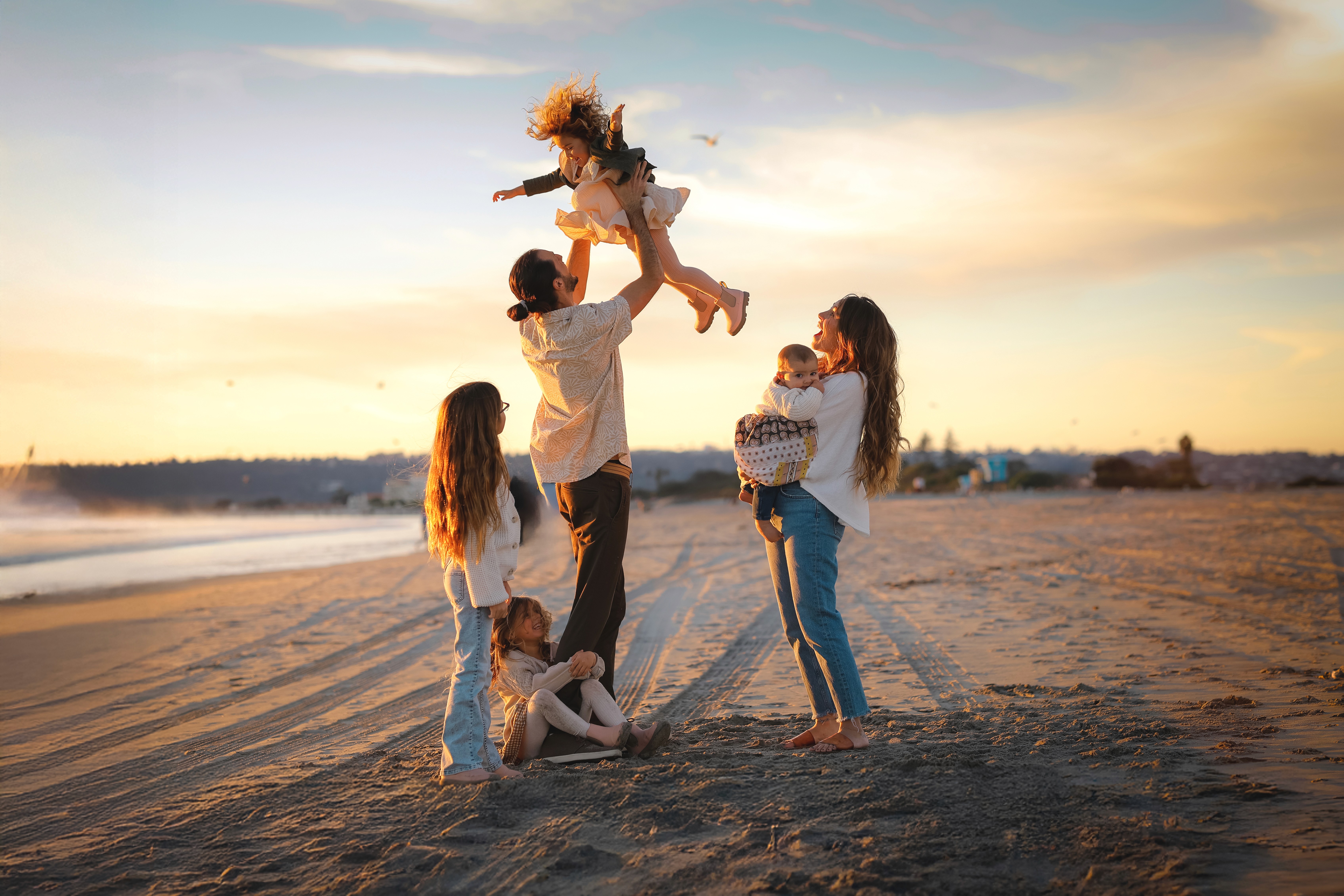 Family holding hands at the shoreline during a family beach session in San Diego.
