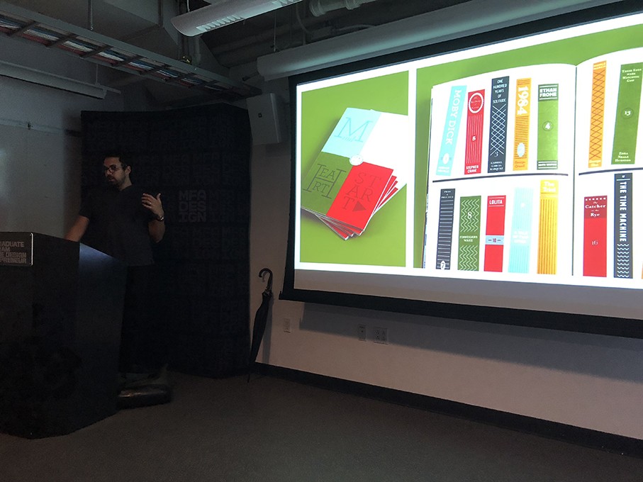 A photo of a man giving a lecture and looking at a projector screen where some yellow, blue, red and green cards are shown.