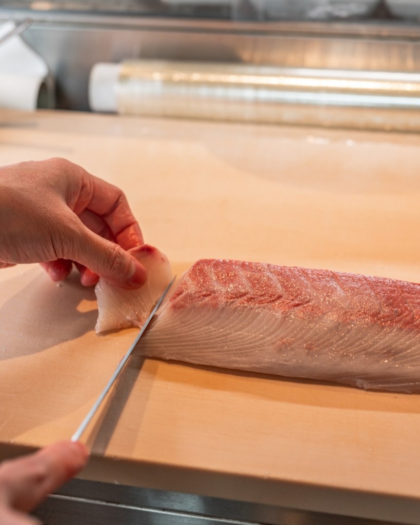 A chef's hand skillfully slicing a fillet of fish on a wooden cutting board.